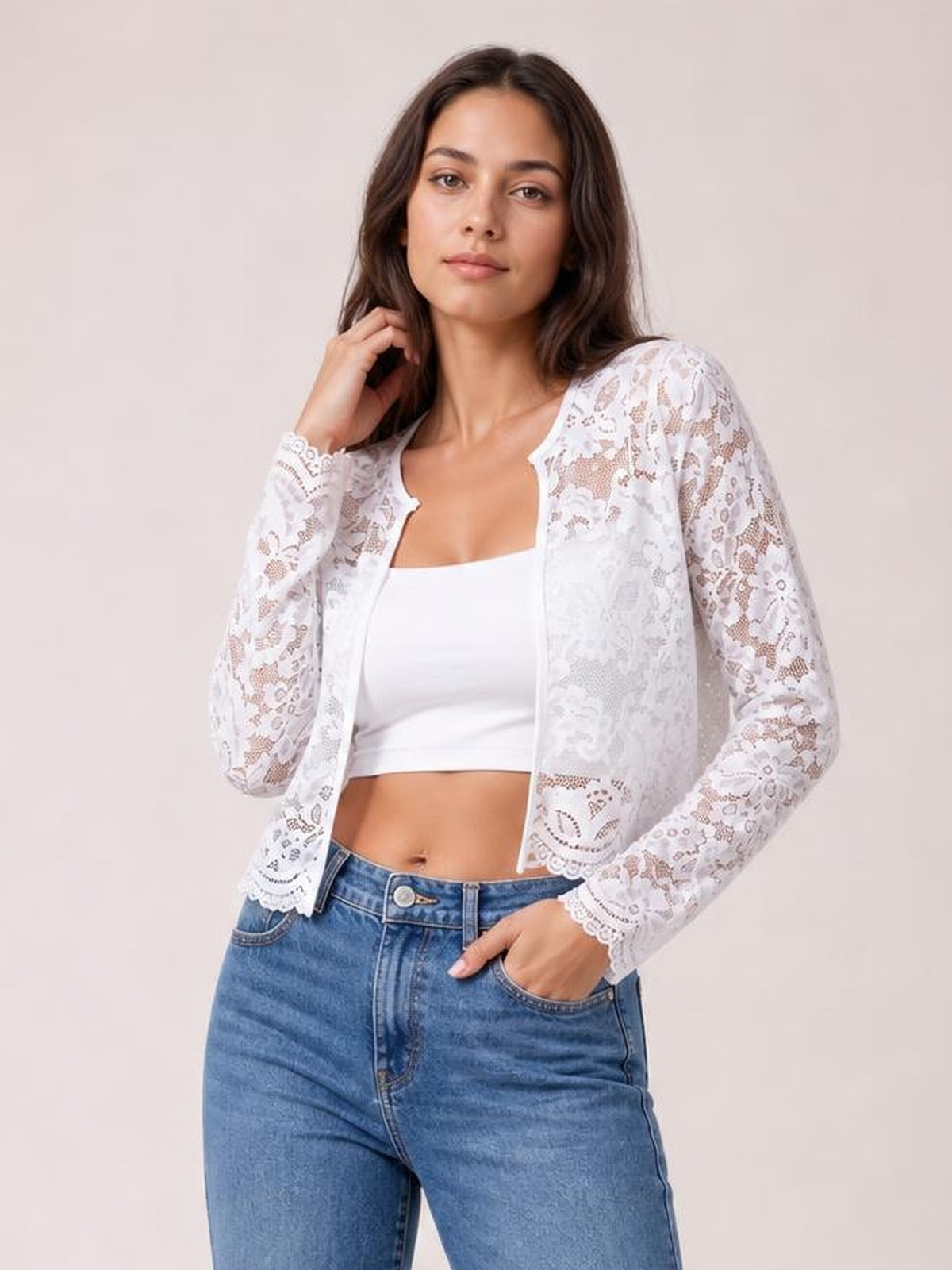 Model wearing a white lace open-front long-sleeve jacket with scalloped edges and a fitted silhouette over a white cropped top and jeans.