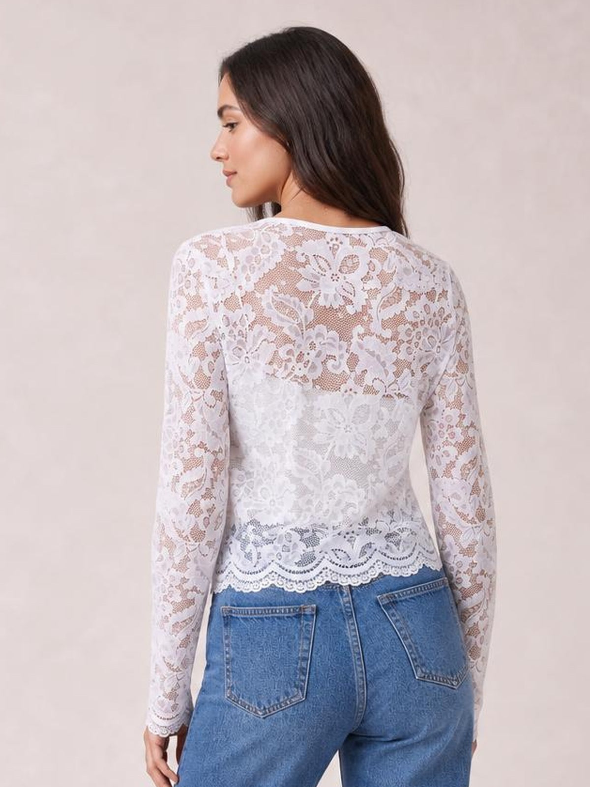 Model turned away in a white floral lace open-front jacket with long sleeves, a fitted silhouette, sheer construction, and scalloped hem.
