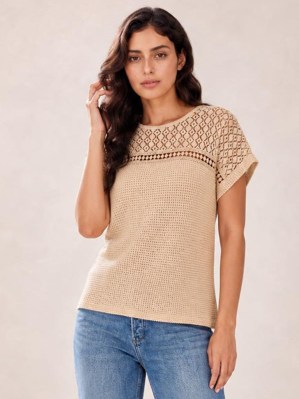 A model touches her hair while wearing a beige lace patchwork waffle knit top with short sleeves, a crew neckline, and a relaxed straight silhouette.