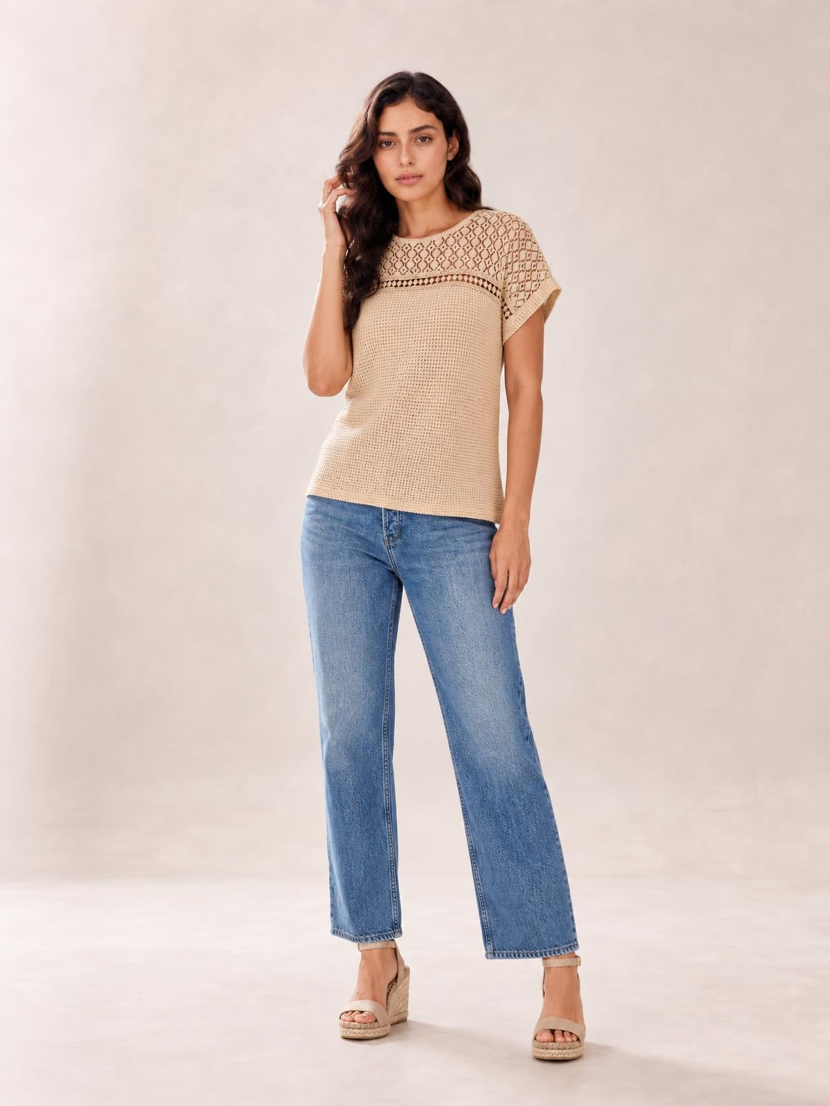 A model touches her hair while wearing a beige lace patchwork waffle knit top with short sleeves, a round neckline, textured yoke, and relaxed straight silhouette.