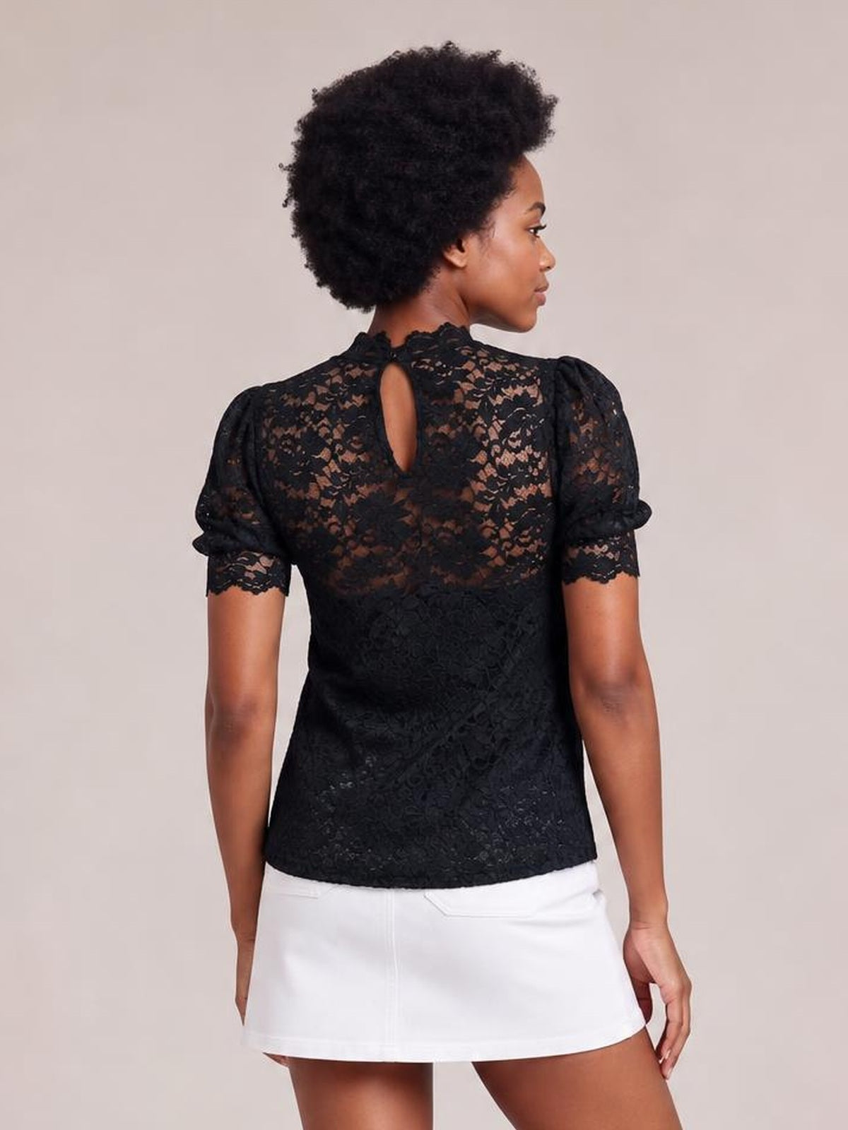 Model shown from the back wearing a black lace scalloped top with a mock neck, short puff sleeves, a keyhole closure, and a regular silhouette.