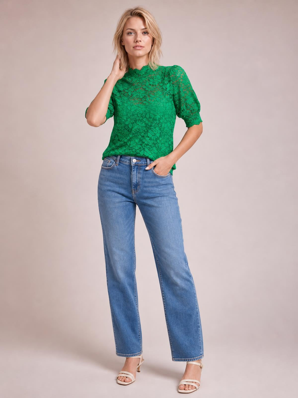 A model wears a green lace top with a mock neck, short puff sleeves, scalloped sleeve edges, and a regular silhouette while posing with one hand in her pocket.