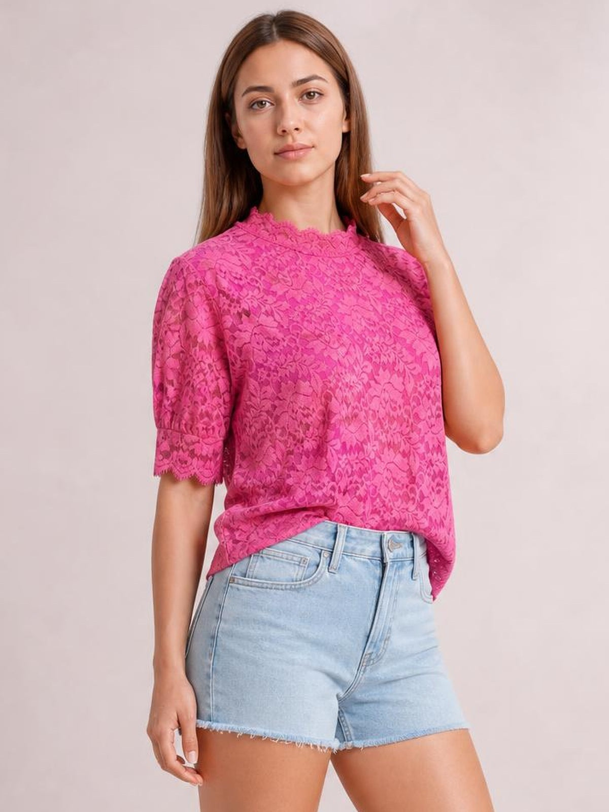 Model wearing a bright pink lace top with a scalloped mock neck, short puff sleeves, scalloped cuffs, and a relaxed regular-fit silhouette.