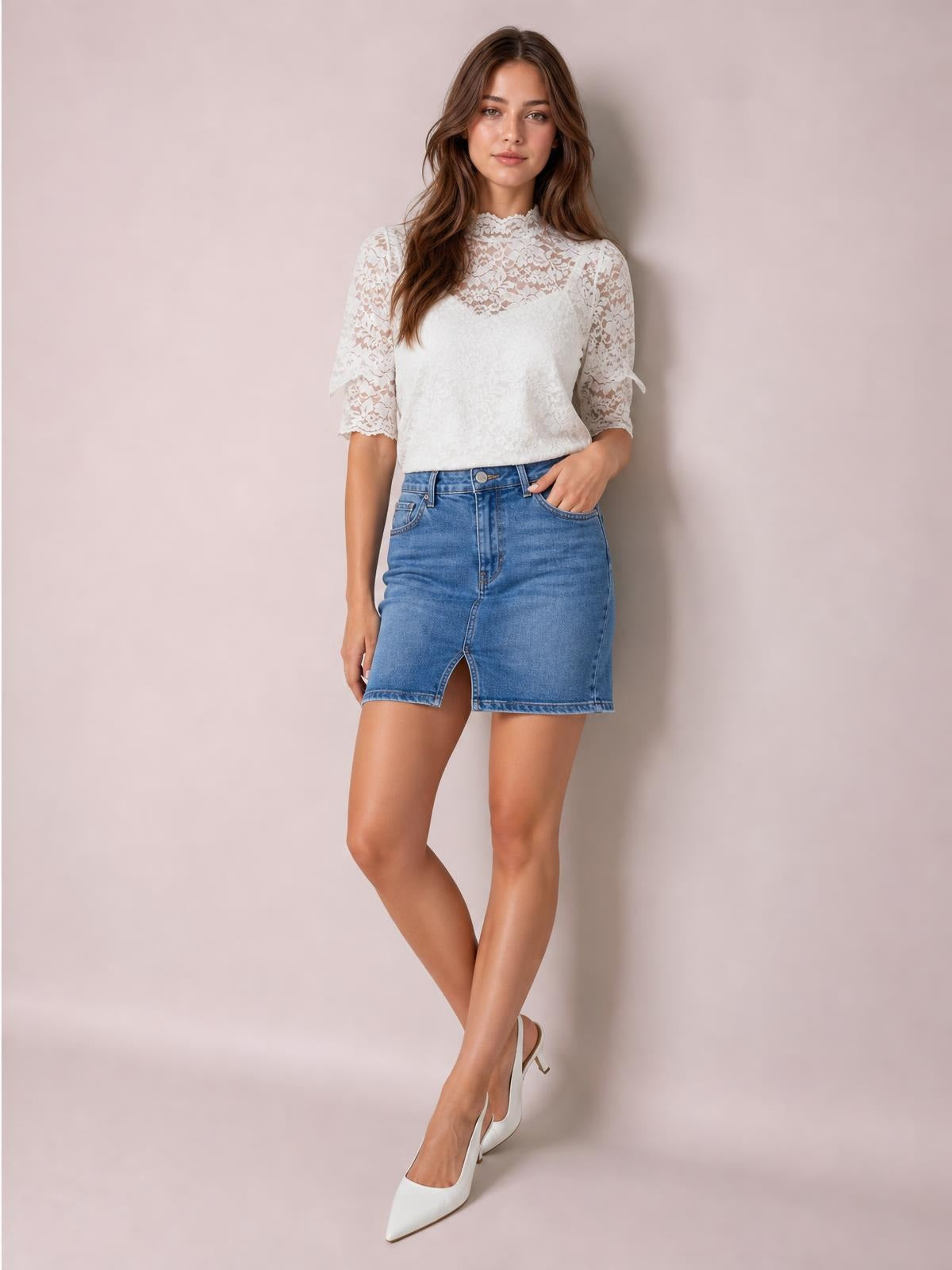 A model poses with one hand in her pocket wearing a white lace top with a mock neck, short puff sleeves, scalloped edges, and a regular silhouette.