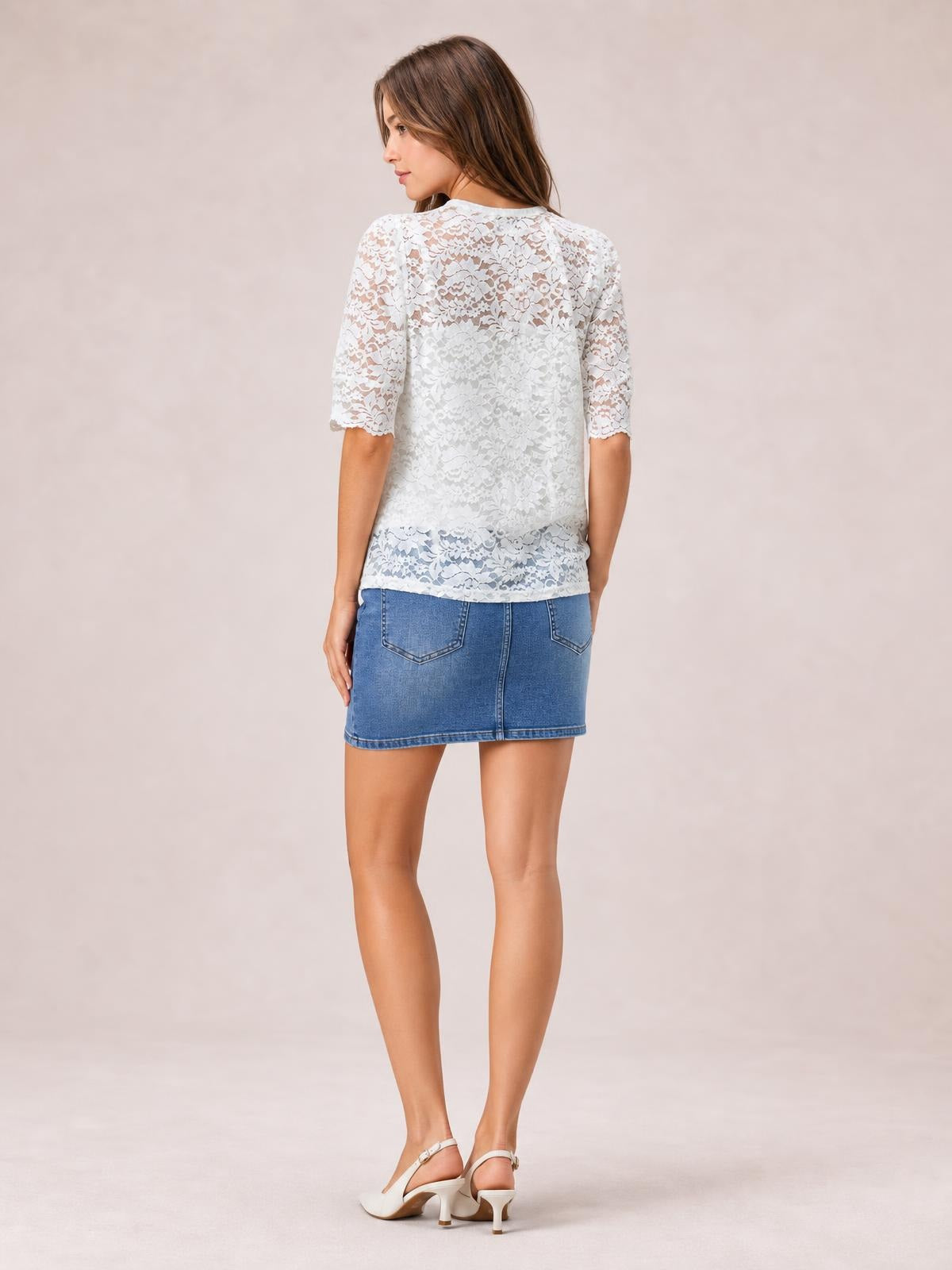 A model looks over her shoulder wearing a white lace top with a regular silhouette, mock neckline, and scalloped short puff sleeves.