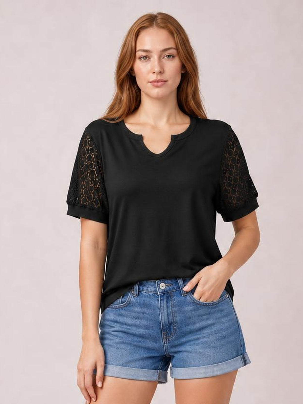 Model wears a black lace short sleeve T-shirt with sheer openwork sleeves, a notched neckline, relaxed silhouette, and one hand in her pocket.