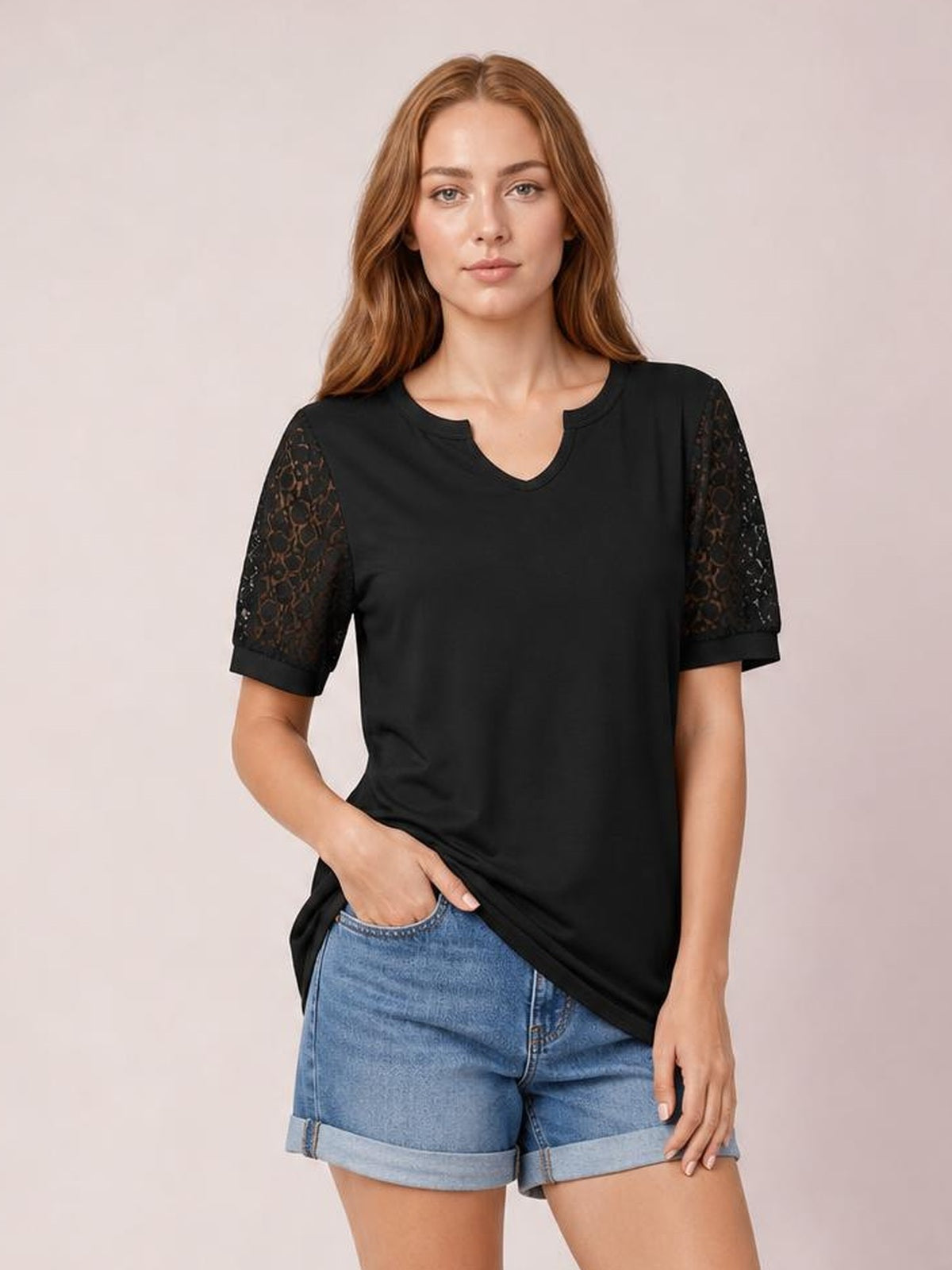 Model poses in a black lace short sleeve T-shirt with semi-sheer openwork sleeves, a notched round neckline, relaxed silhouette, and hem held at the hip.