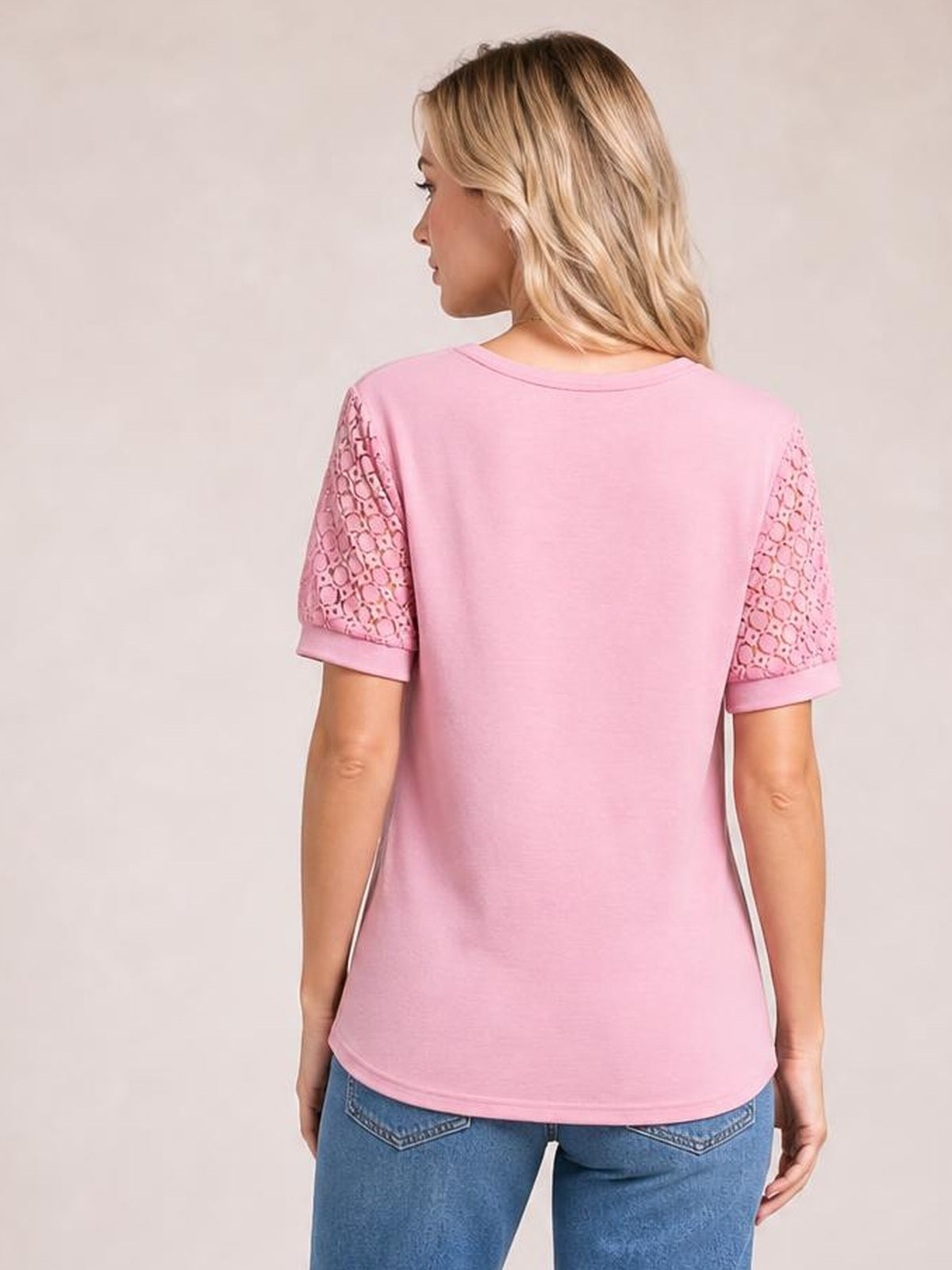 Model turned away in a pink lace short sleeve T-shirt with semi-sheer openwork sleeves, ribbed cuffs, a crew neckline, and a relaxed straight silhouette.