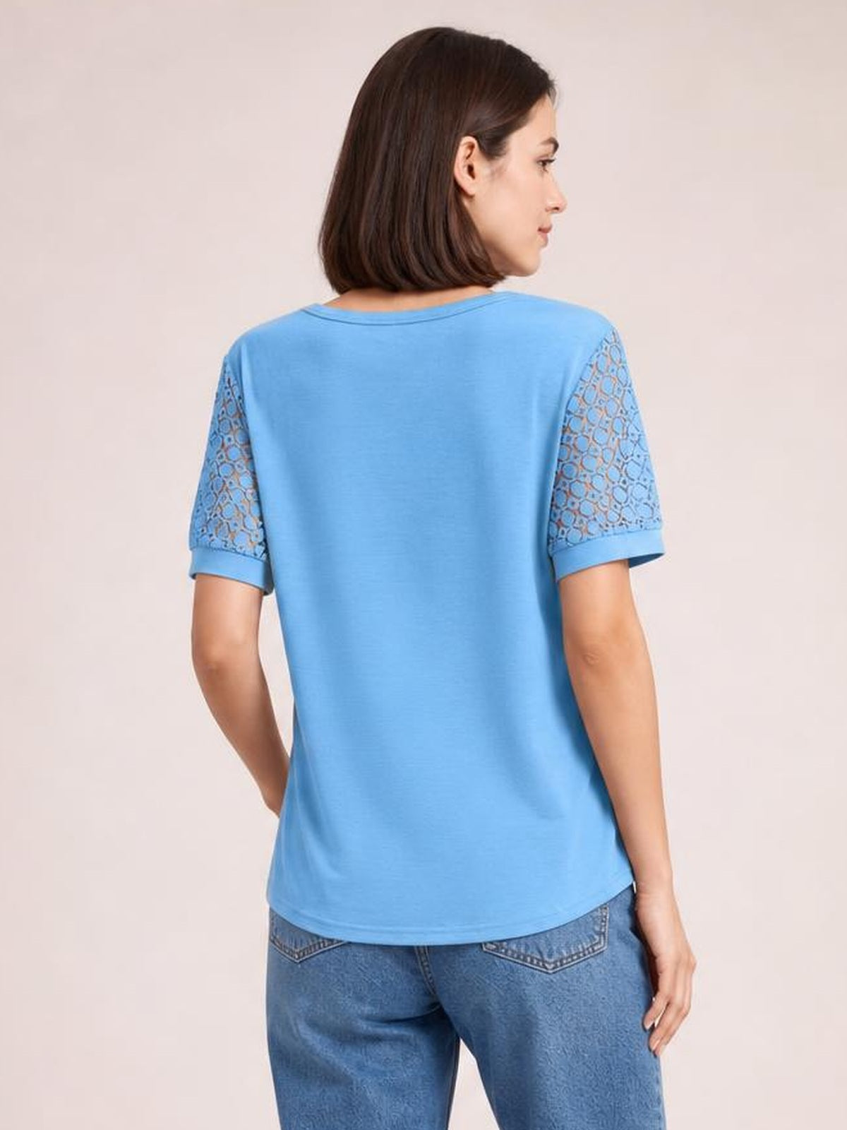 Model shown from the back in a blue lace short sleeve T-shirt with semi-sheer openwork sleeves, a relaxed silhouette, and slightly curved hem.