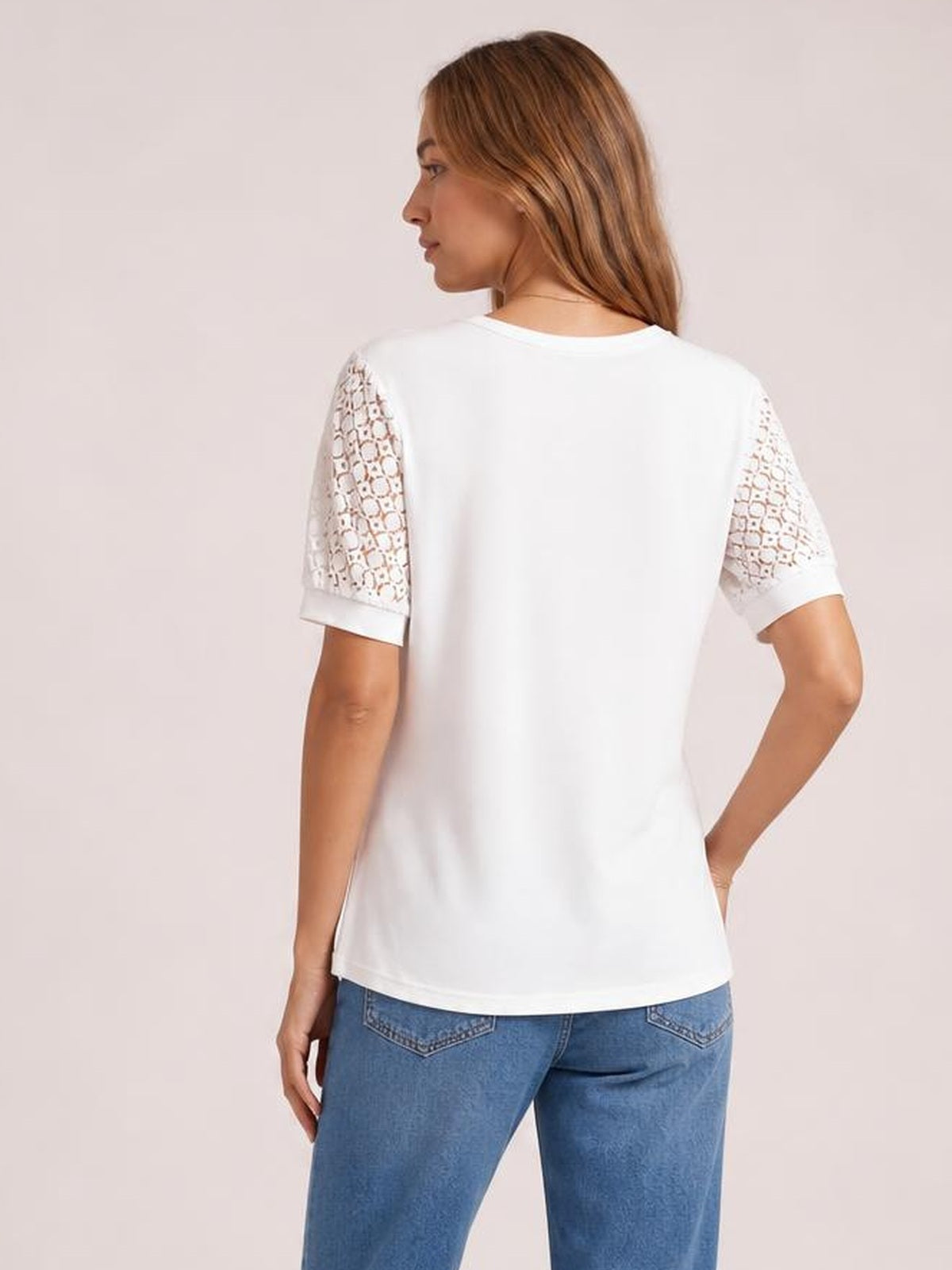 Model in a back three-quarter pose wears a white short-sleeve T-shirt with semi-sheer lace openwork sleeves, ribbed cuffs, and a relaxed straight silhouette.