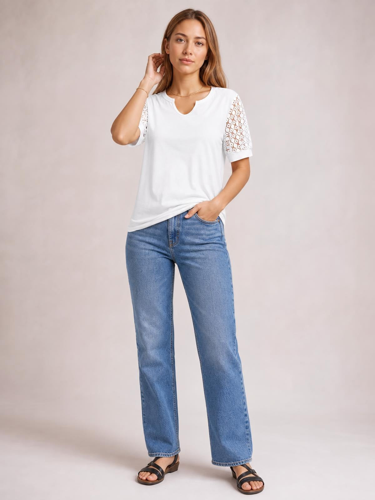 Model wearing a white lace short sleeve T-shirt with semi-sheer openwork sleeves, a relaxed silhouette, and a notched neckline, posing with one hand in her jeans pocket.