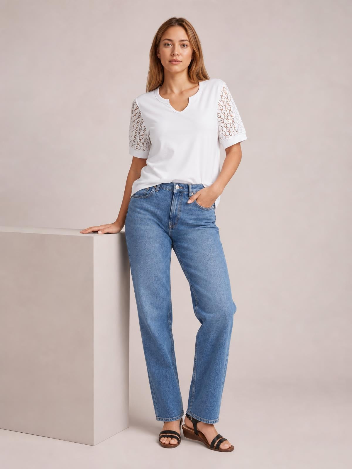A model wears a white Lace Short Sleeve T-Shirt with semi-sheer openwork lace sleeves, a relaxed silhouette, and a notched neckline while posing in jeans.