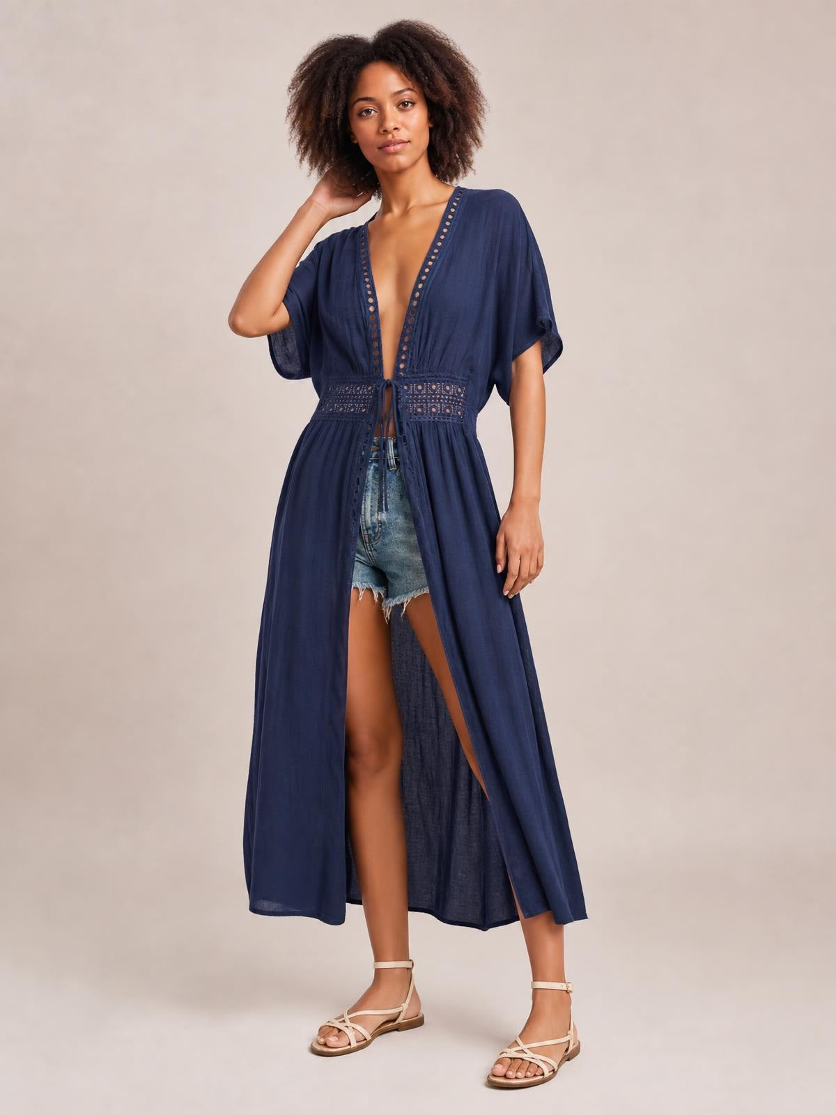 A model poses in a navy sheer beach cover-up maxi dress with a plunging V-neck, lace trim, short sleeves, tied waist, and flowing open-front silhouette.