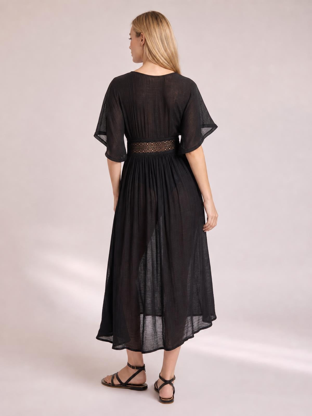 Back view of a model in a black sheer beach cover-up maxi dress with flutter sleeves, lace-trimmed tie waist, and a flowing full-length silhouette.