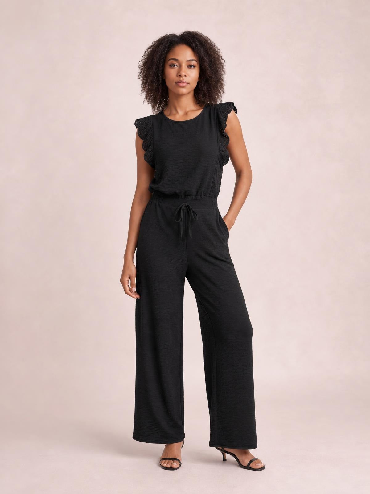 Model poses in a black lace-trim round-neck top and matching wide-leg pants set, featuring ruffled sleeves, a tied waist, and a relaxed silhouette.