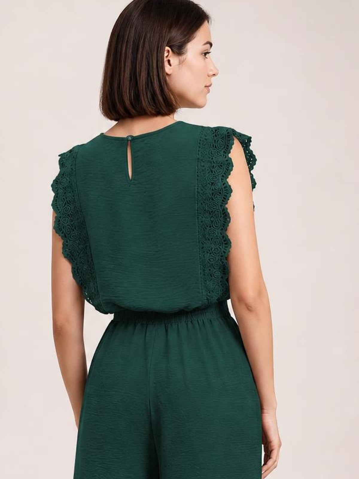 A model turned away wears a dark green round-neck top and matching pants set with lace-trimmed flutter sleeves, a back keyhole closure, and a relaxed silhouette.