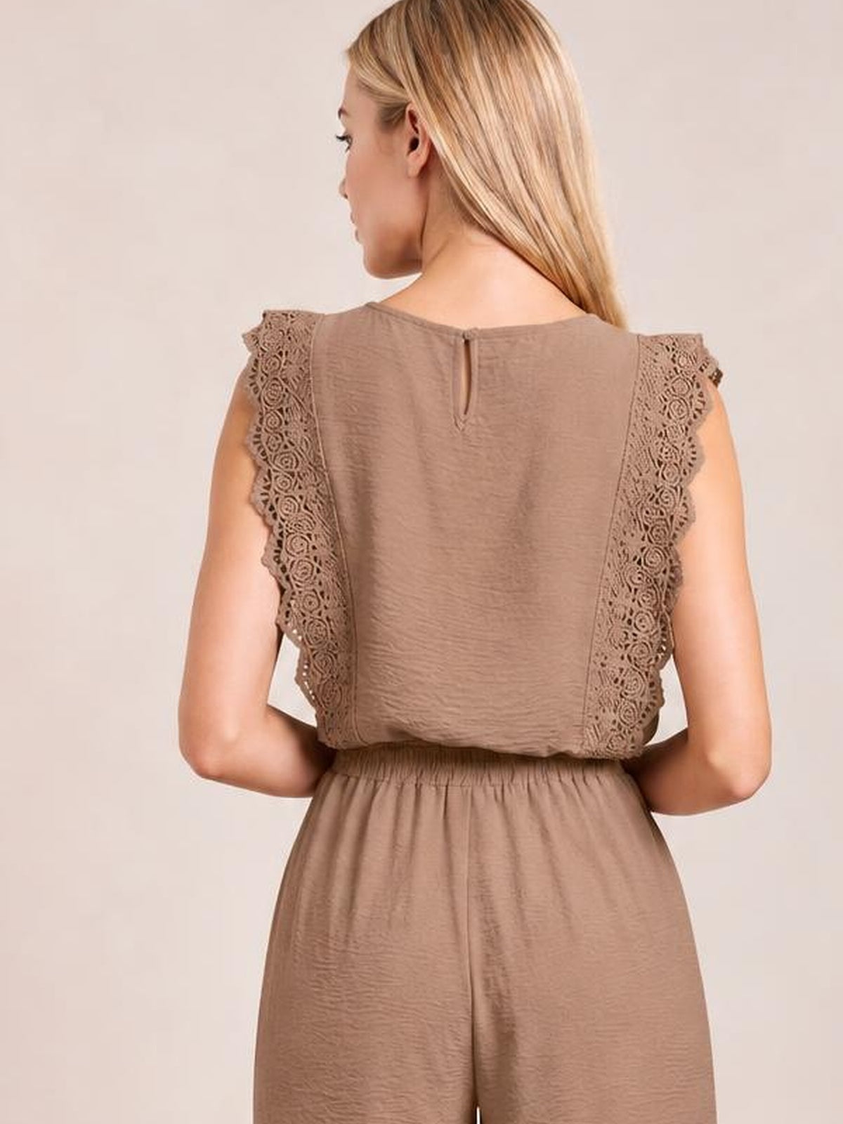 A model wears a taupe lace-trim round-neck top and matching relaxed pants, shown from behind with scalloped cap sleeves and a neat waistline.