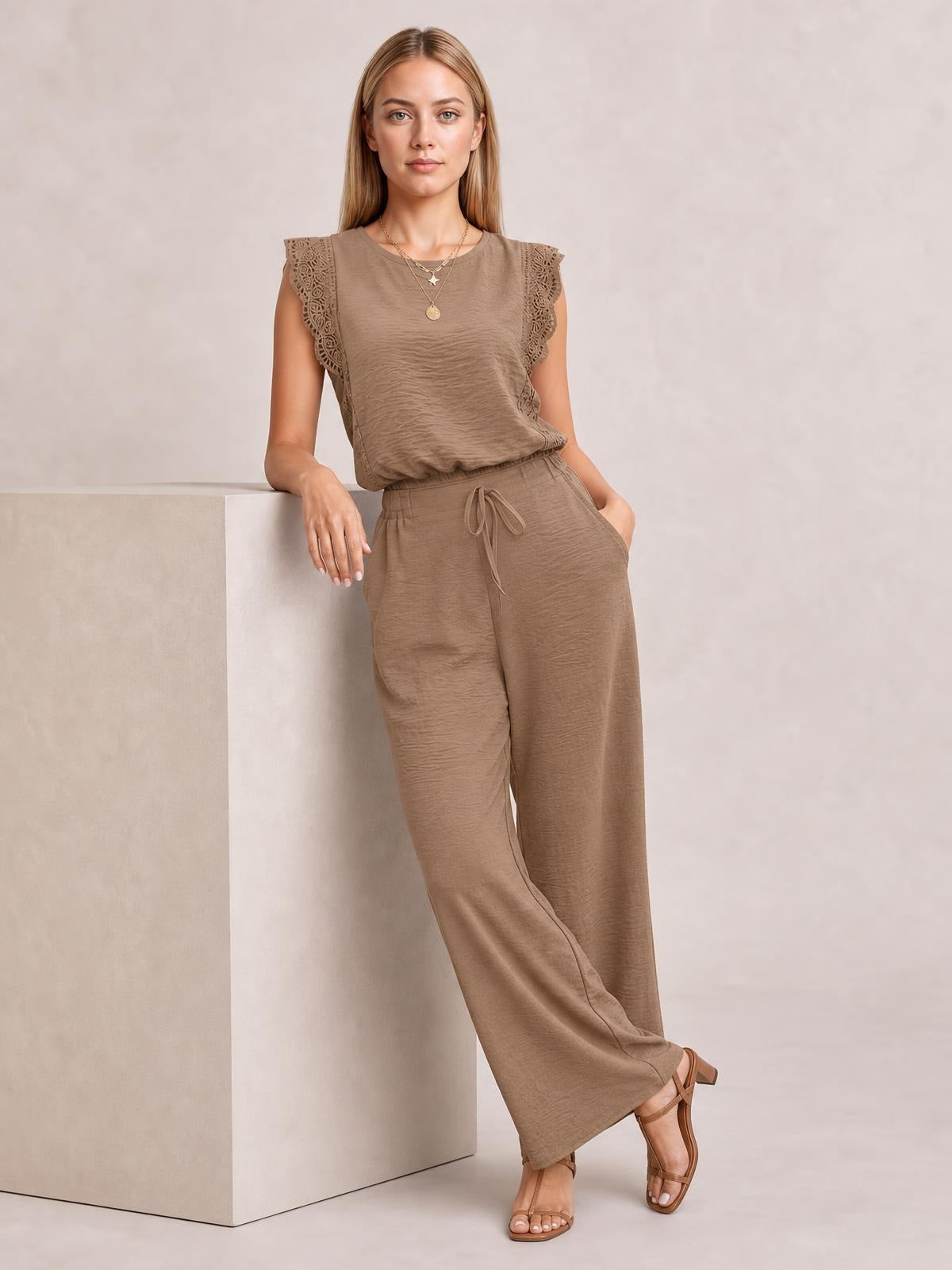 A model leans casually in a taupe lace-trim round-neck top and matching wide-leg pants set with a tied drawstring waist.