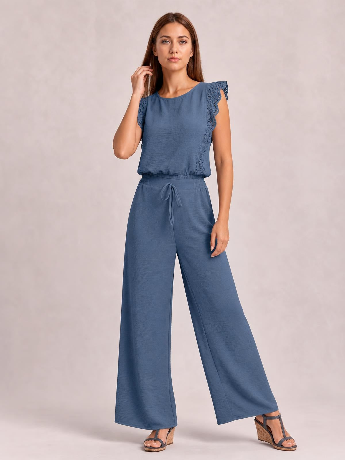 A woman poses in a blue round-neck top with lace-trimmed ruffled shoulders and tied waist, paired with matching wide-leg pants.