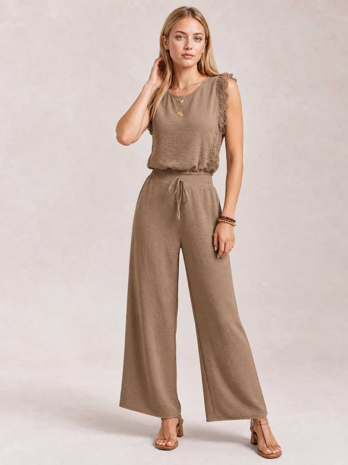 Model poses in a taupe round-neck top with scalloped lace-trim shoulders and tied waist, paired with matching wide-leg pants for a coordinated silhouette.