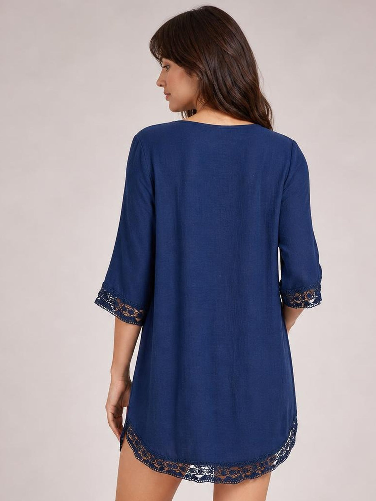Model shown from behind in a navy blue cover-up with a relaxed, long silhouette, three-quarter sleeves, and delicate lace trim at the cuffs and curved hem.