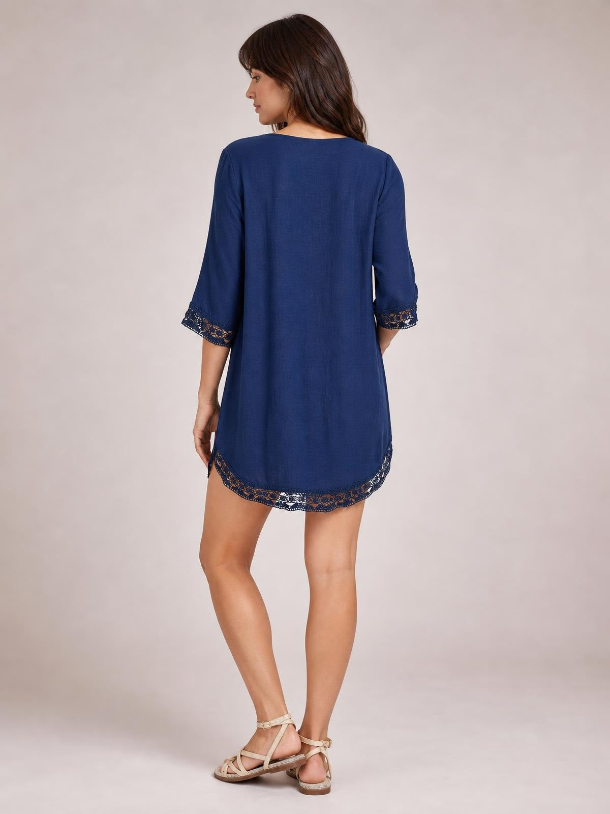 Model poses in a back view wearing a navy lace trim cover-up with a relaxed silhouette, three-quarter sleeves, and delicate lace edging at the cuffs and hem.