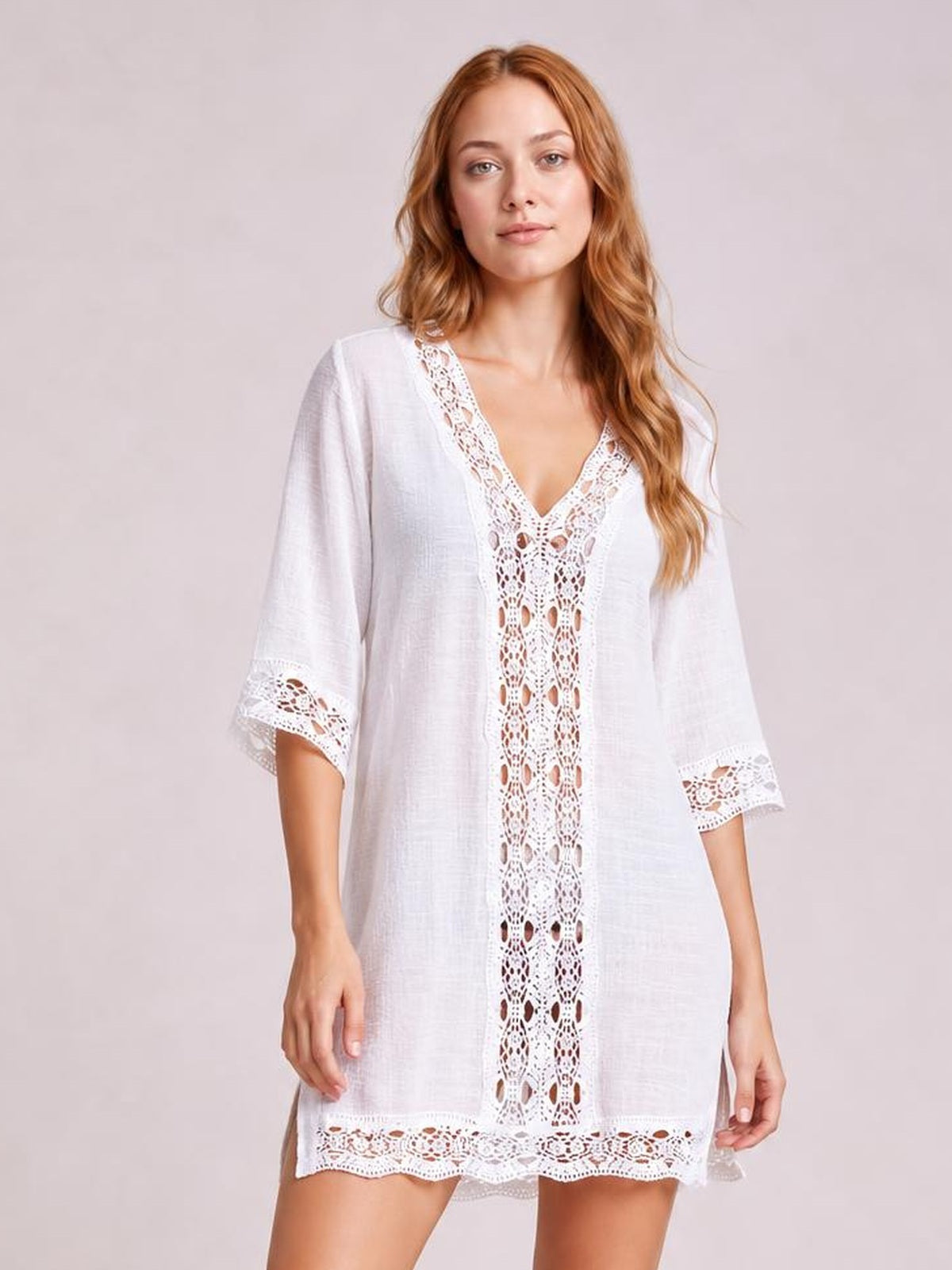 Model poses in a white loose-fit V-neck cover-up with intricate lace trim along the neckline, front panel, three-quarter sleeves, and hem.