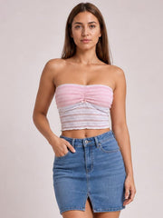 A model poses with one hand in her pocket wearing a pink lace tube top with a ruched center, strapless neckline, and fitted cropped silhouette.