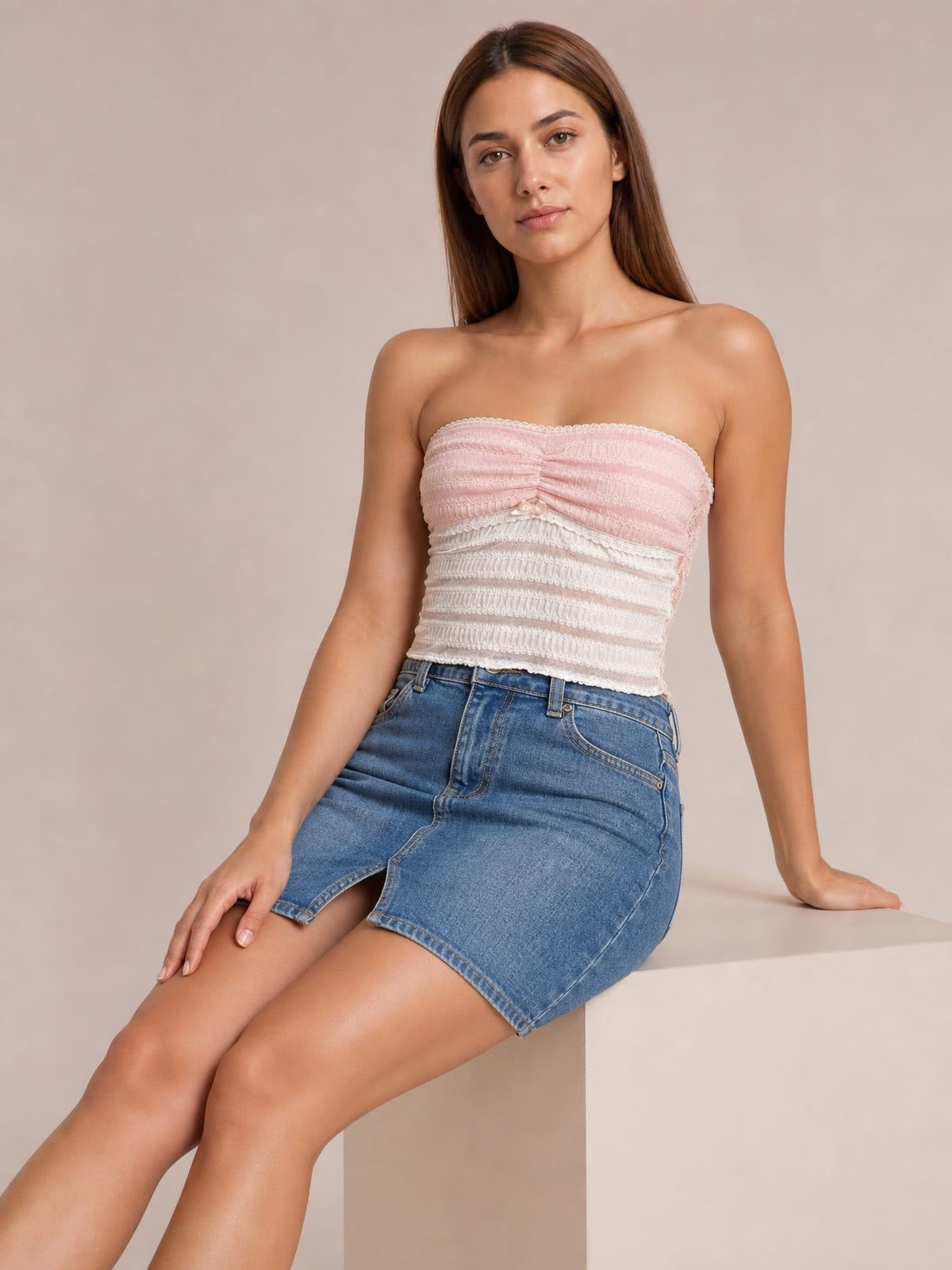 A model sits in a fitted lace tube top with ruched construction, a pale pink and white design, and a strapless silhouette.