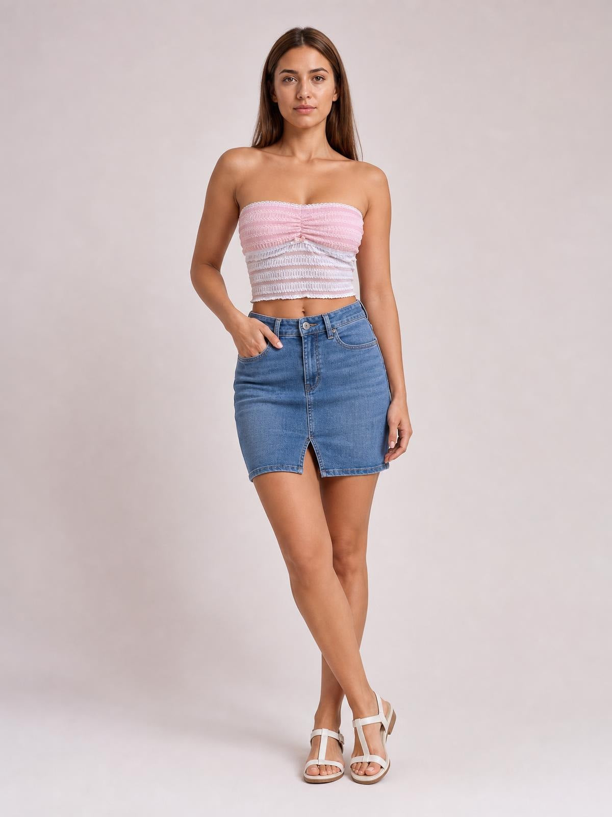 Model poses with one hand in her pocket wearing a pink and white ruched lace tube top with a strapless cropped silhouette and slightly stretchy fit.