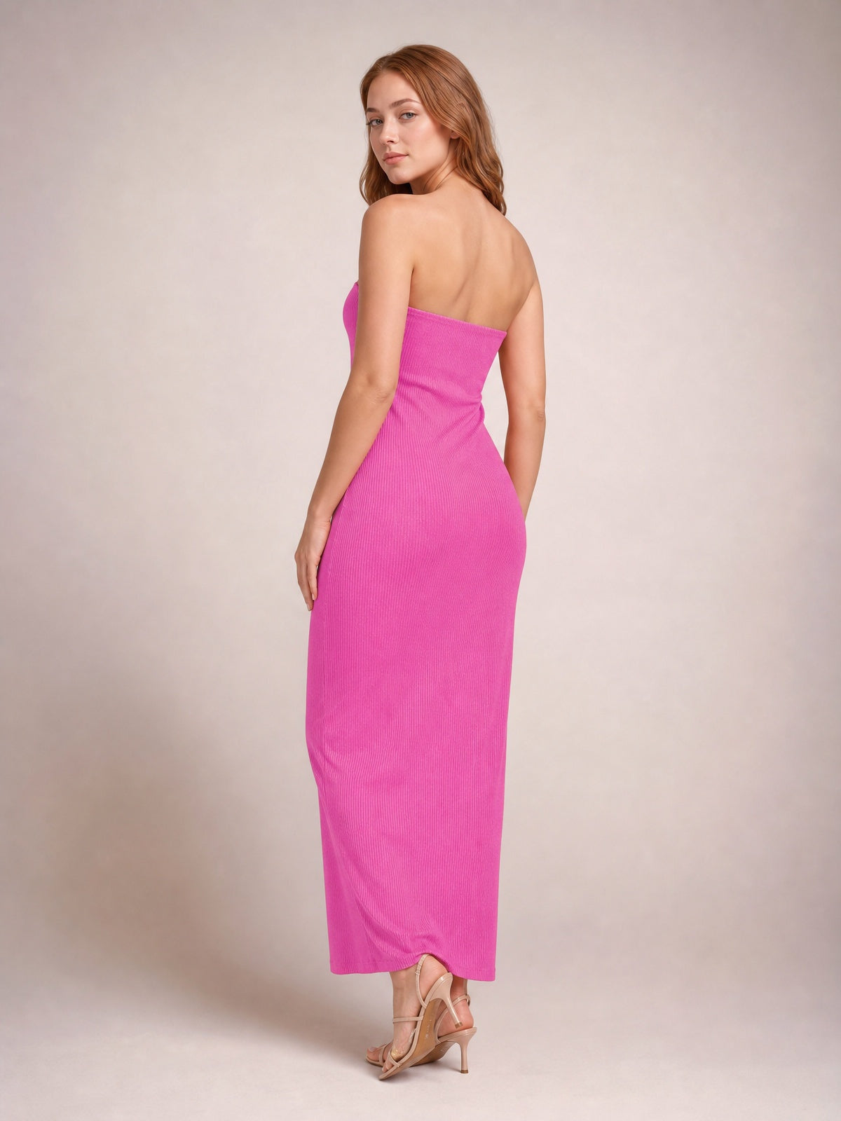 A model looks over her shoulder in a bright pink strapless maxi dress with an open back, ribbed texture, and a sleek body-skimming column silhouette.