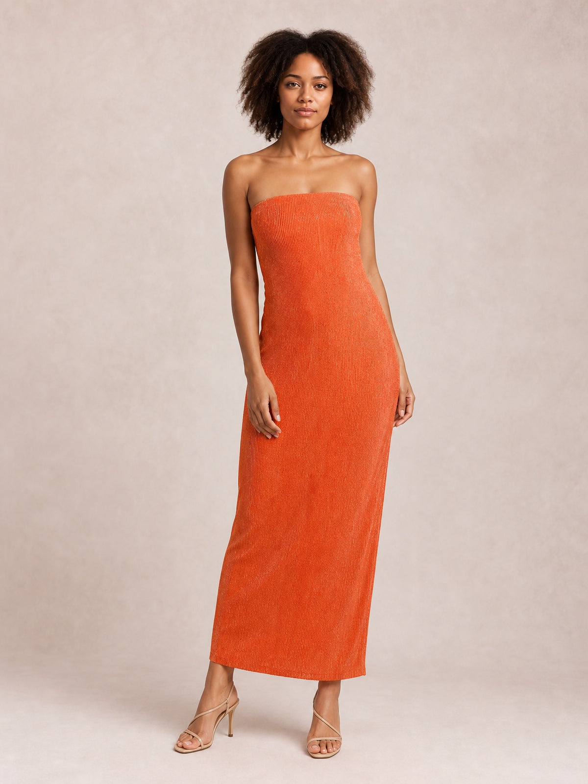 A model stands in a bright orange tube maxi dress with a strapless neckline, textured fabric, and a sleek, body-skimming column silhouette.