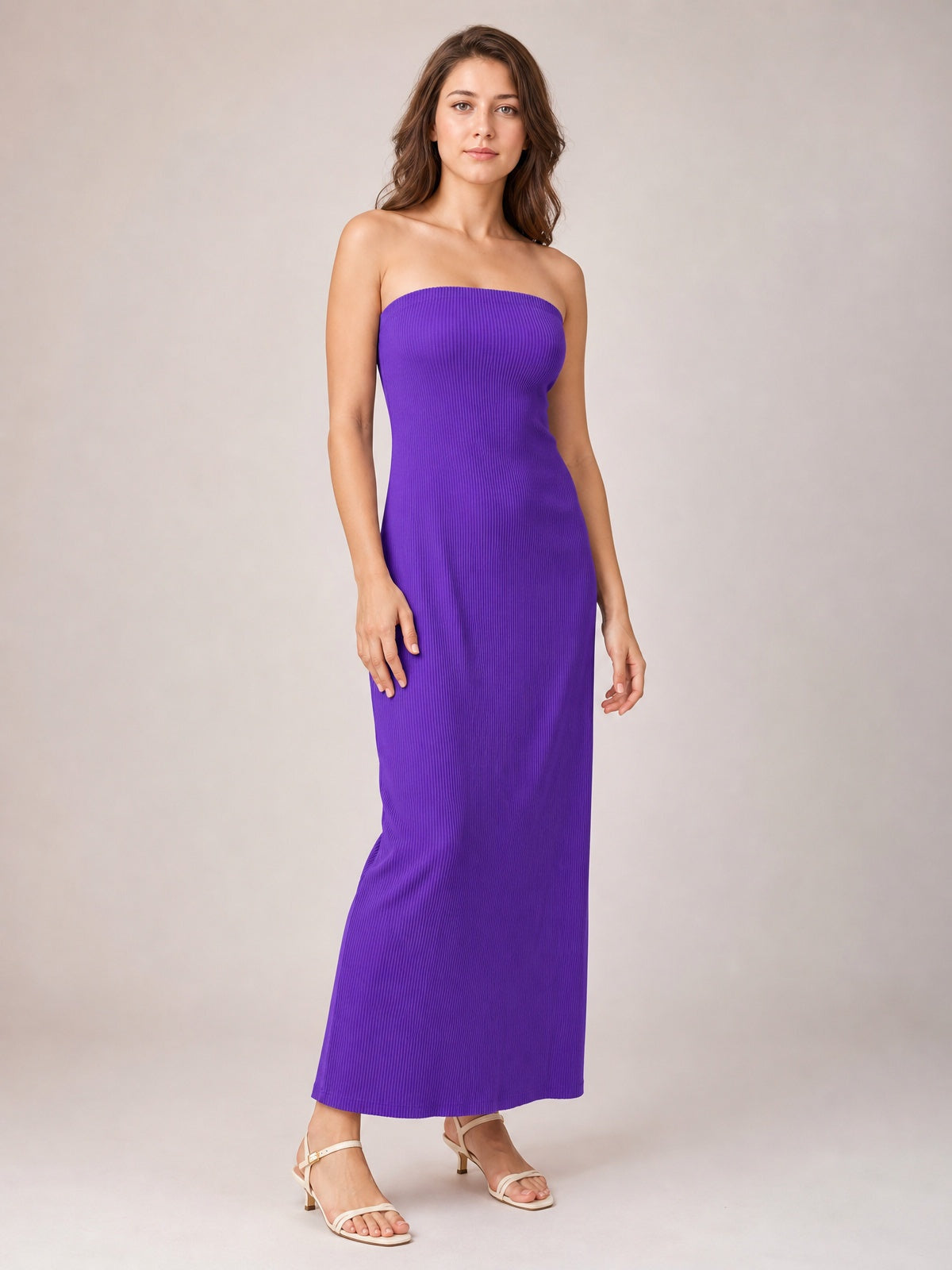 A model stands in a vibrant purple tube maxi dress with a strapless neckline, fine vertical texture, and a sleek, body-skimming column silhouette.