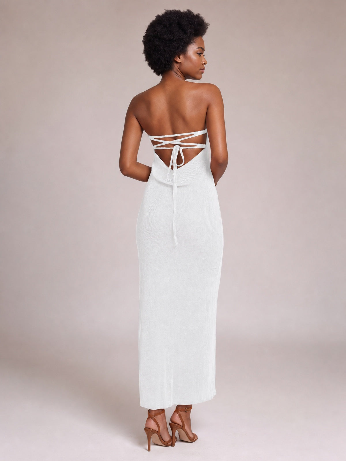 A model looks over her shoulder in a white strapless tube maxi dress with a body-skimming column silhouette and open lace-up back.