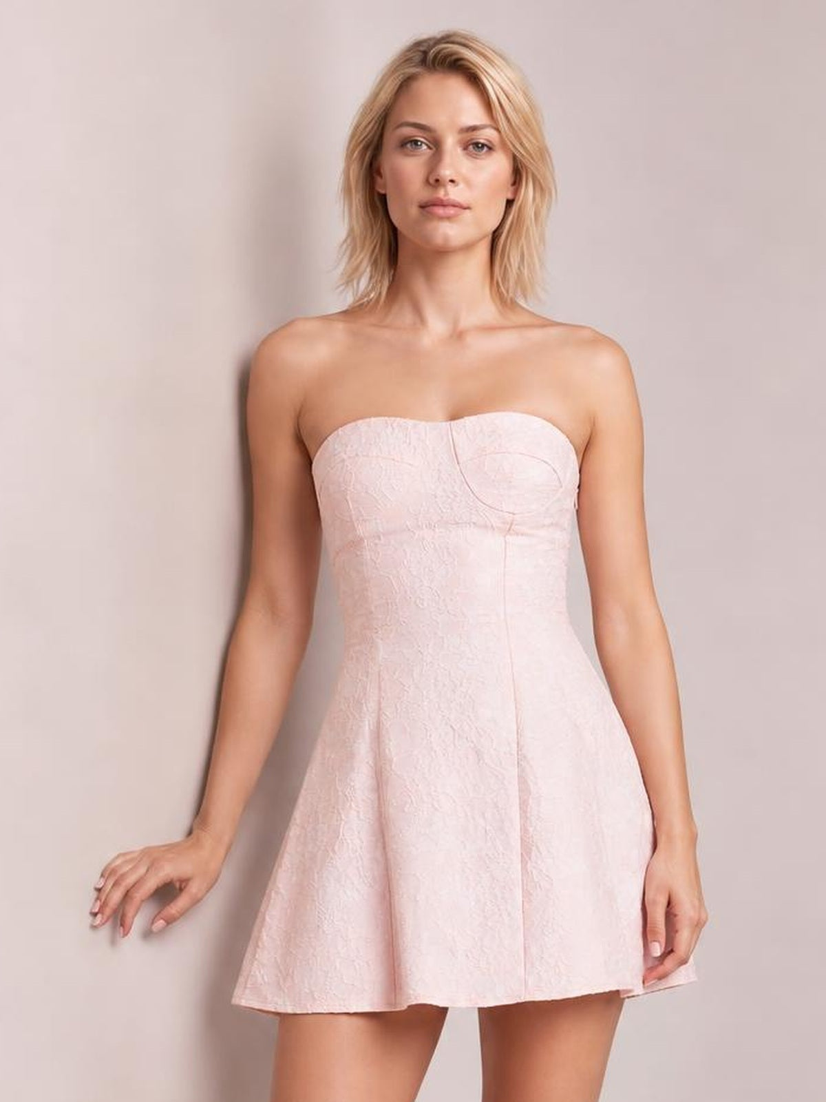 Model wears a pale pink lace-up jacquard tube mini dress with a strapless structured bodice, curved neckline, fitted waist, and flared lined skirt.