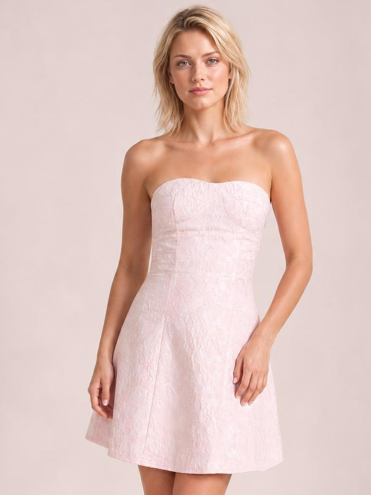 A model stands in a pale pink jacquard tube mini dress with a strapless straight neckline, fitted bodice, and gently flared skirt.
