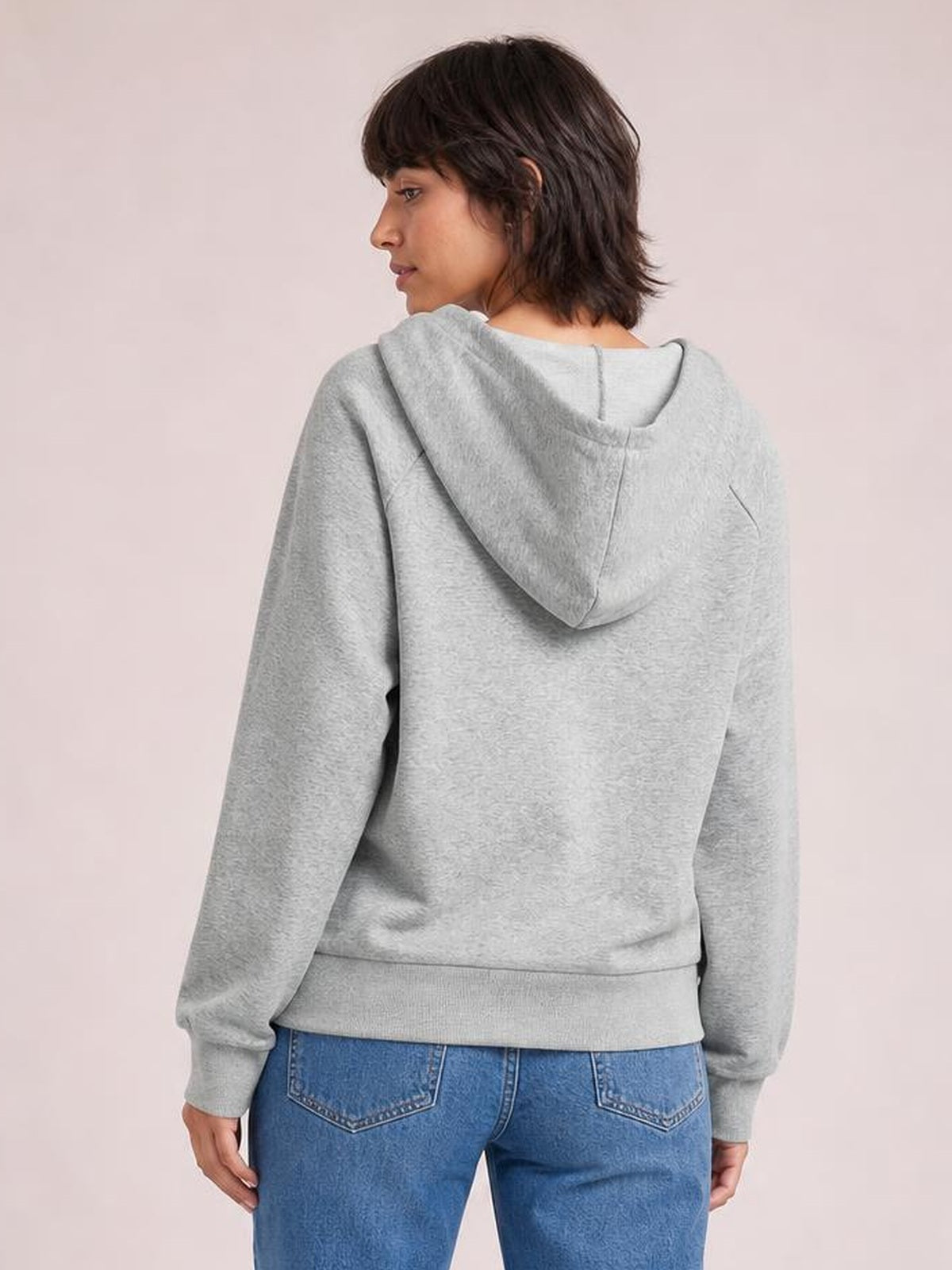 Model shown from behind wears a light gray long sleeve hoodie with a relaxed silhouette, attached hood, ribbed cuffs, and a ribbed waistband.