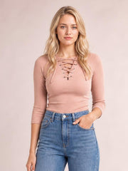 A model poses in a fitted blush pink ribbed long-sleeve T-shirt with a crisscross lace-up chest detail and slightly stretchy silhouette.