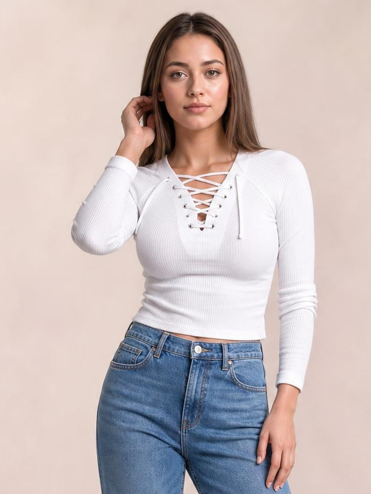 Model poses in a fitted white ribbed long sleeve T-shirt with a crisscross lace-up neckline and slightly cropped silhouette.