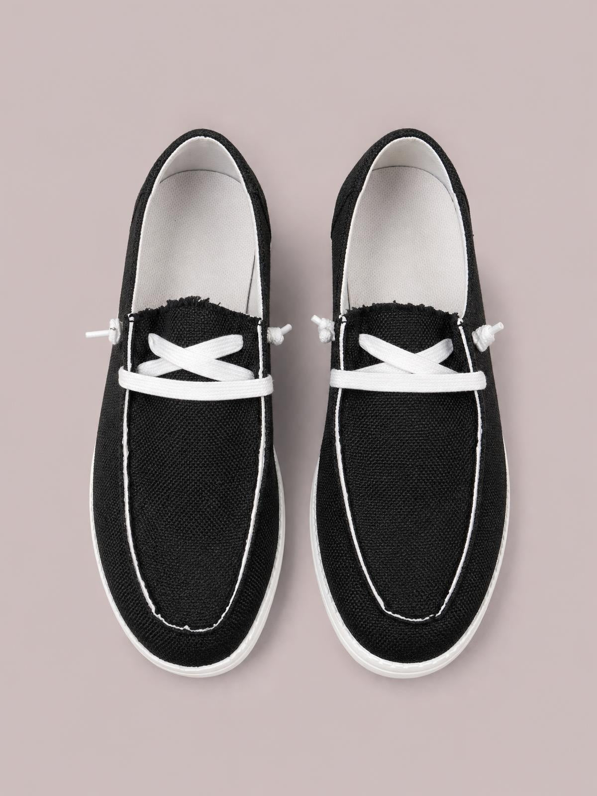 Black canvas lace-up round-toe slip-ons with white contrast stitching, woven laces, and flat white rubber soles.