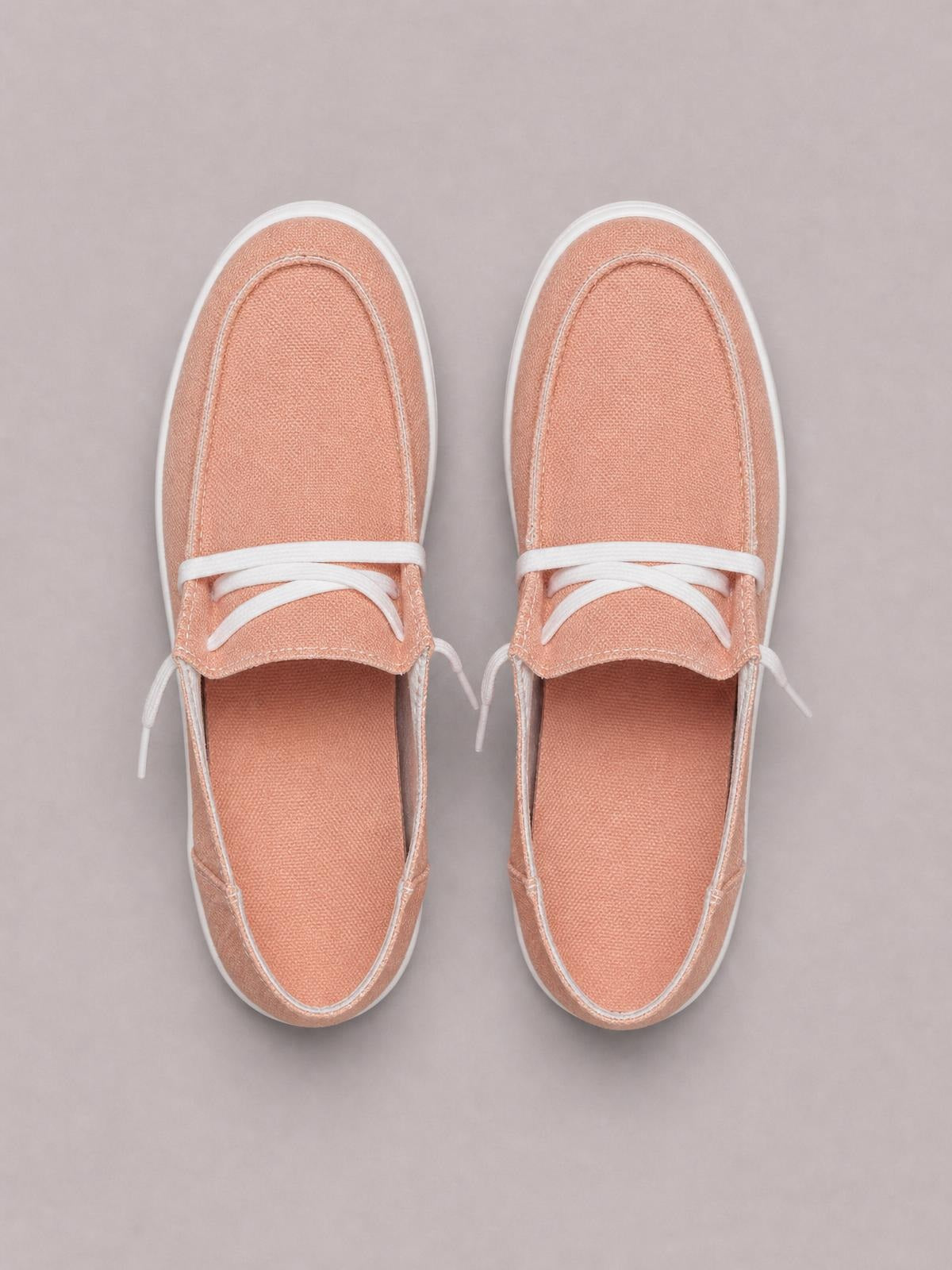 Peach canvas round-toe lace-up slip-ons feature white contrast stitching and flat white rubber soles in an overhead view.