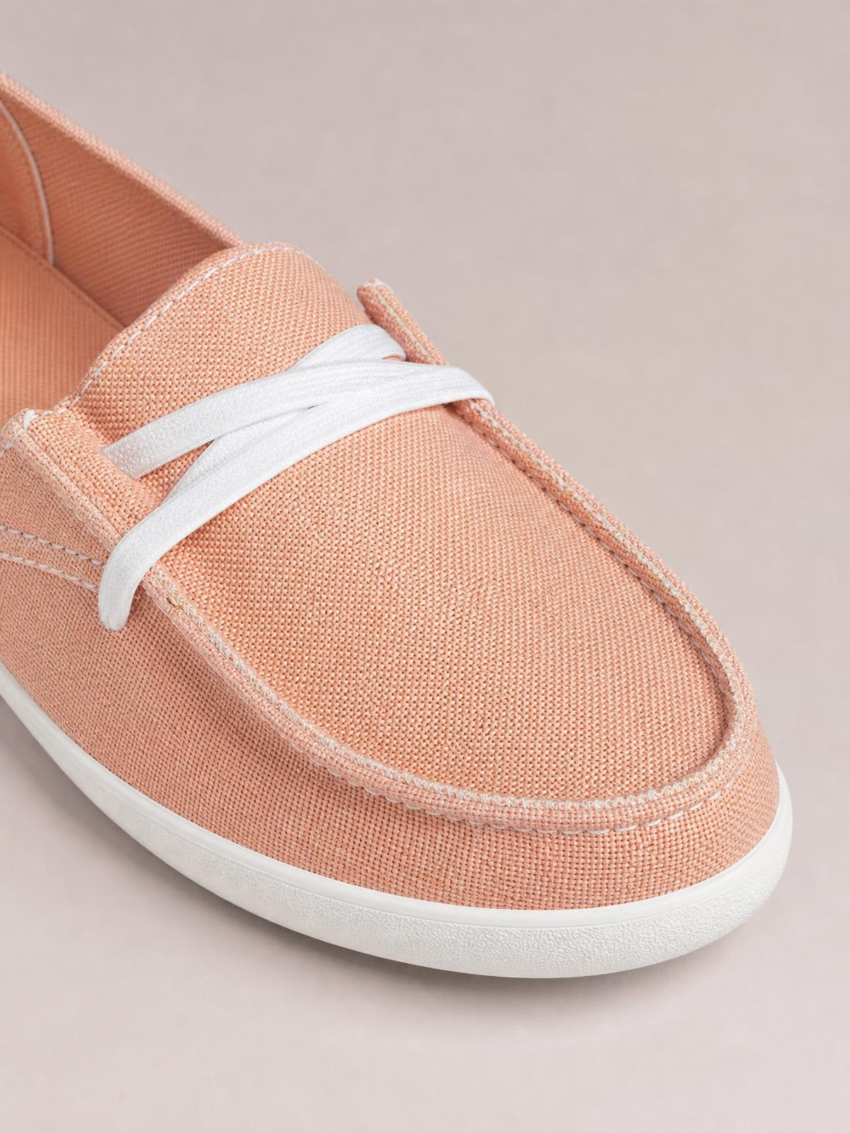 Peach canvas lace-up round-toe slip-ons feature white crossing laces, stitched paneling, a low flat silhouette, and a white rubber sole.