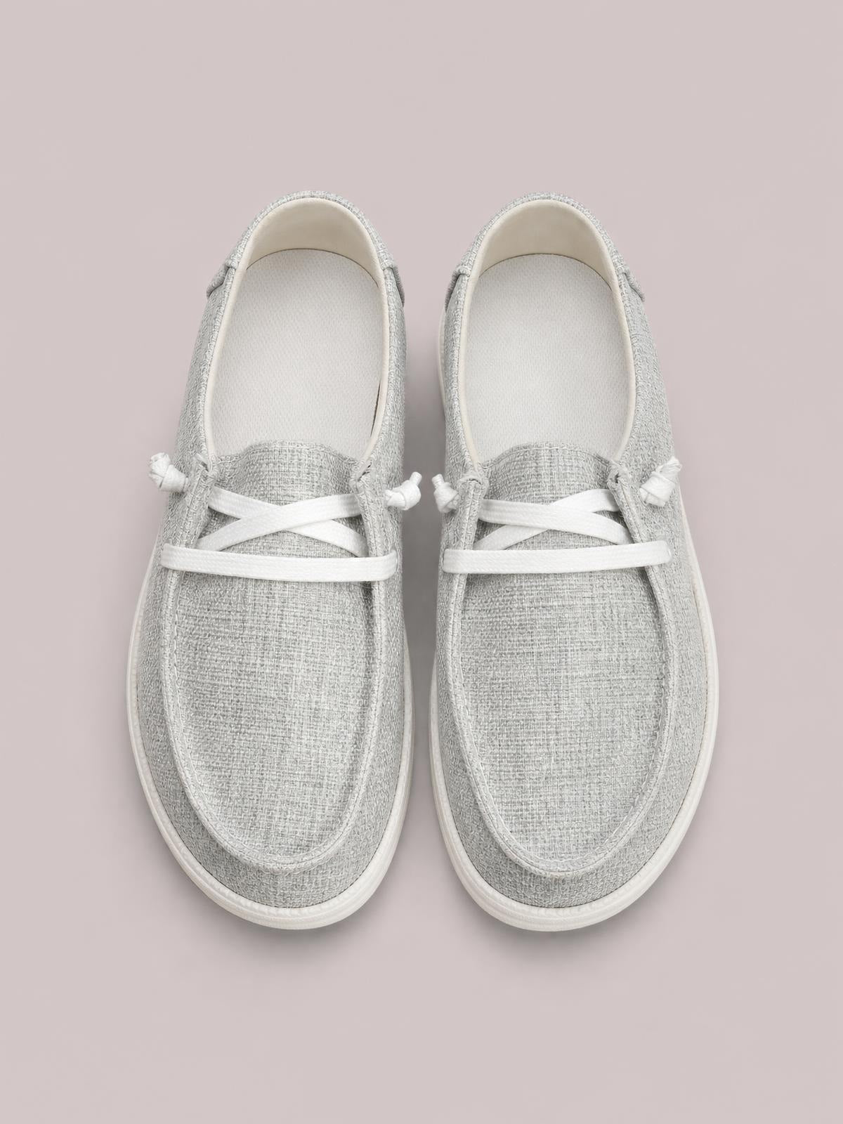 Gray canvas round-toe slip-ons feature white crisscross laces, stitched toe overlays, padded openings, and flat white rubber soles.