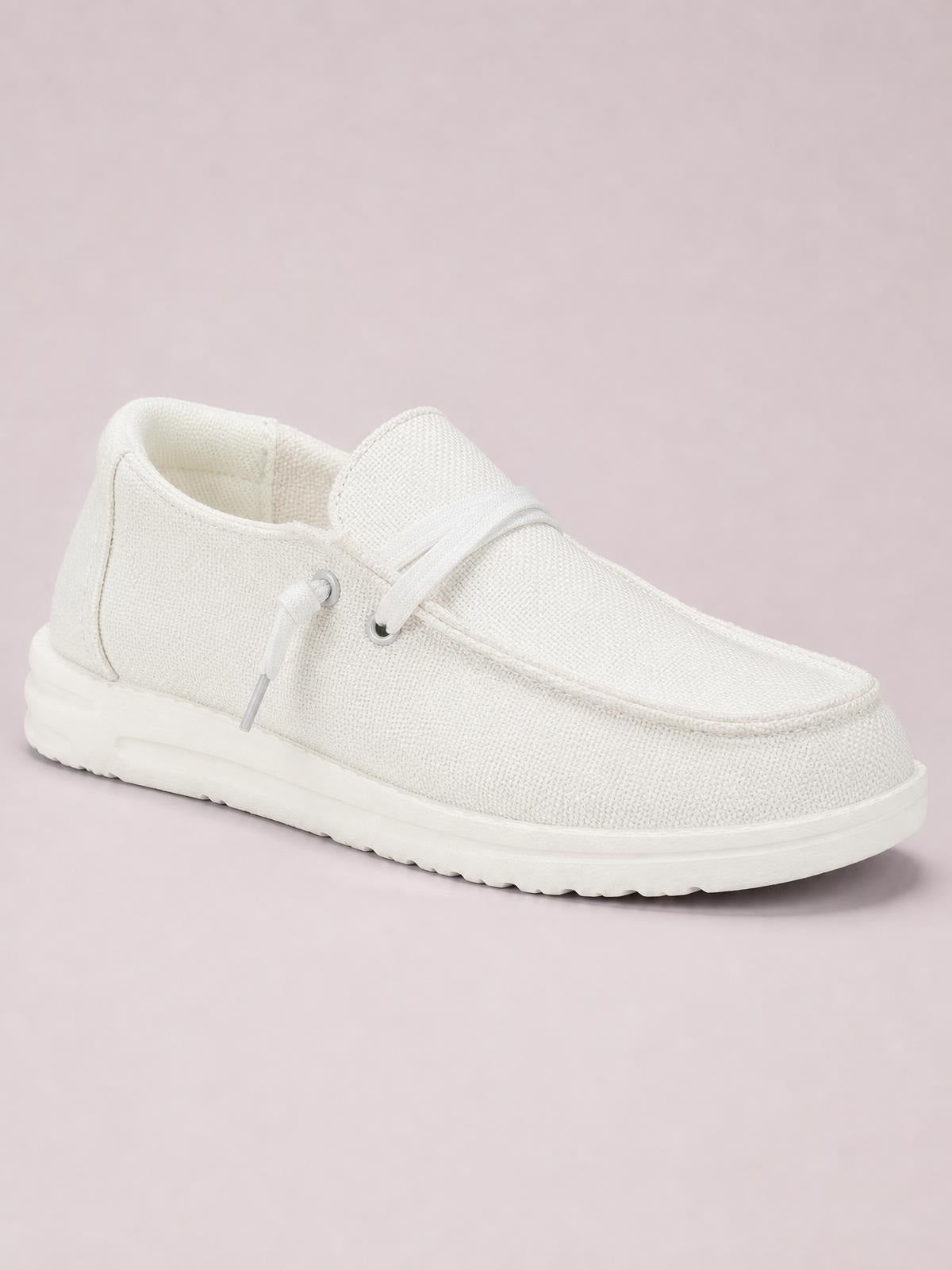White canvas lace-up slip-on shoes feature a rounded moc toe, low flat profile, padded collar, and thick textured rubber sole.
