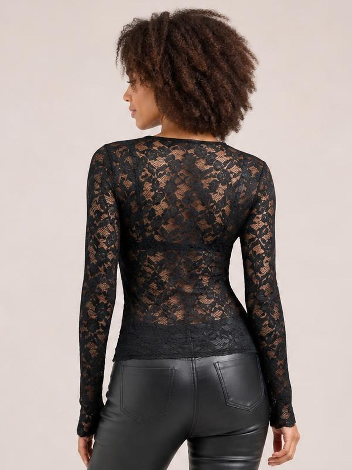Model shown from the back wearing a fitted black sheer lace top with long sleeves, a floral pattern, and a gently shaped waist.
