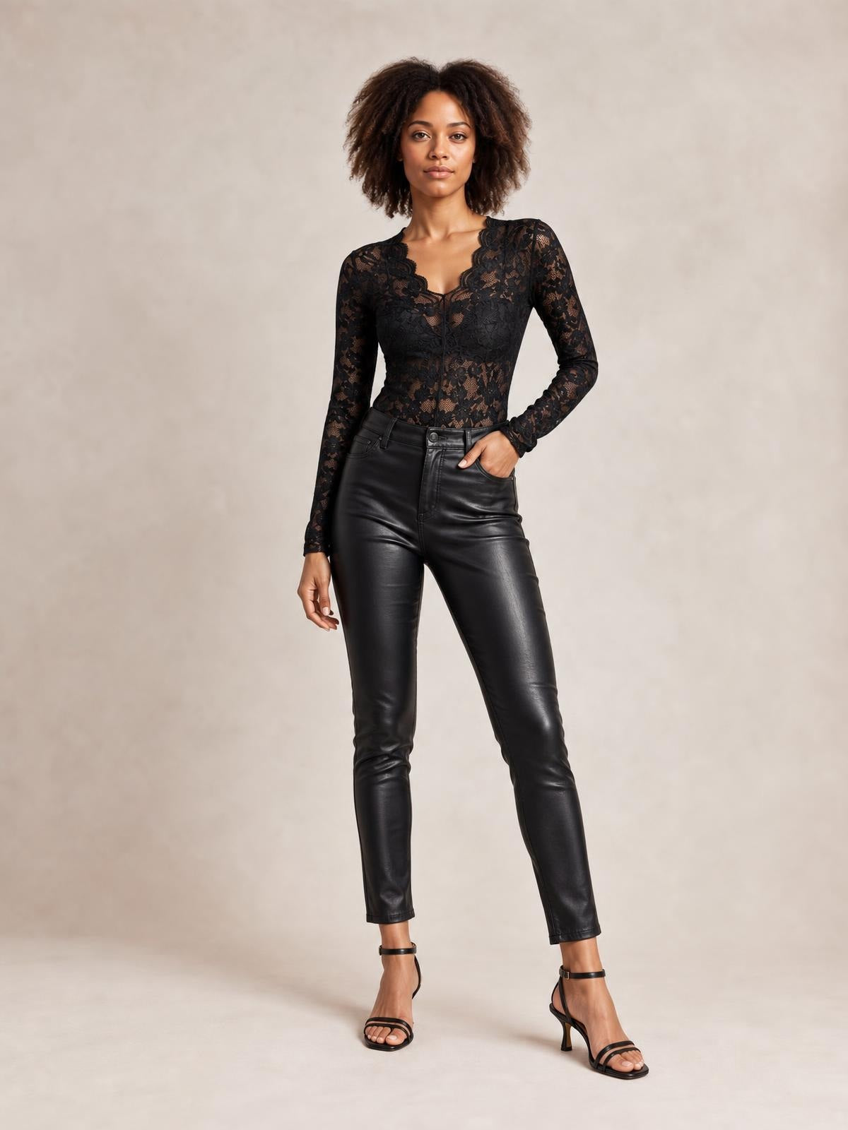 Model poses in a black sheer lace V-neck long sleeve top with a fitted silhouette and floral construction, paired with black pants.