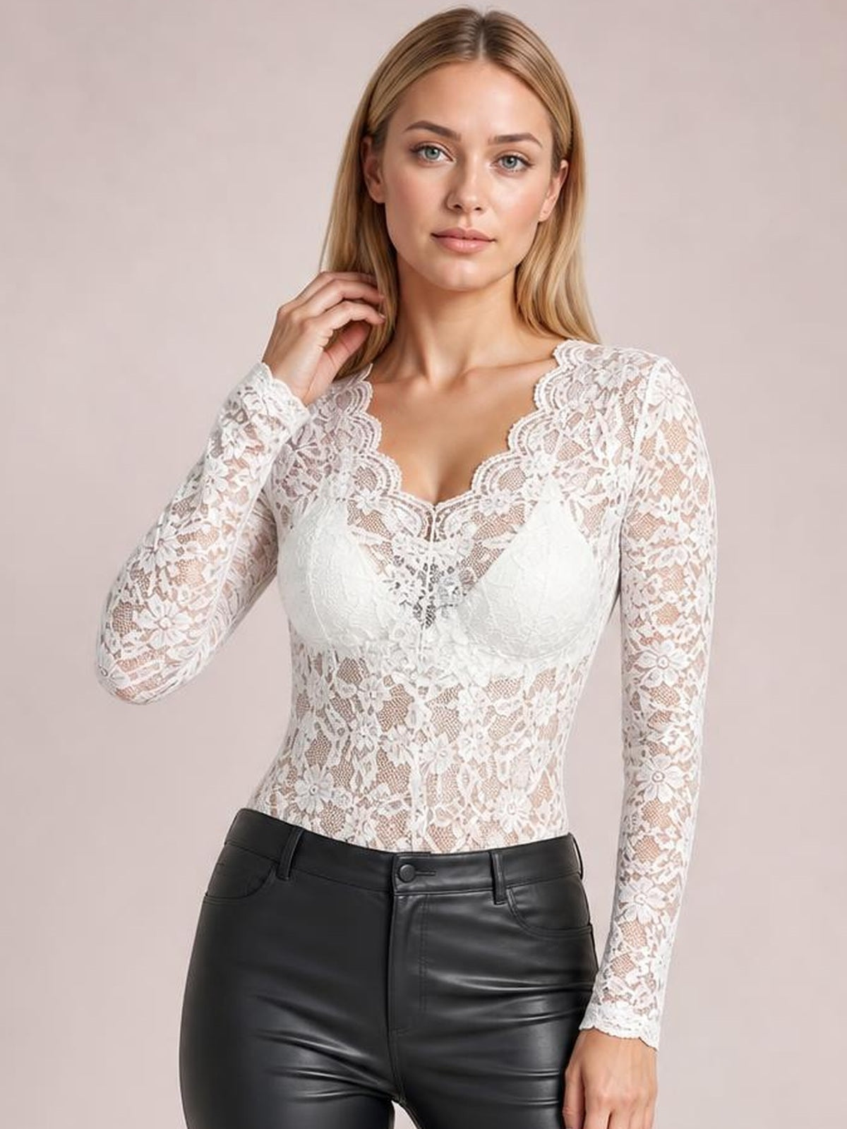 Model wearing a fitted white sheer lace V-neck long sleeve top with floral construction, posing with one hand near her hair.