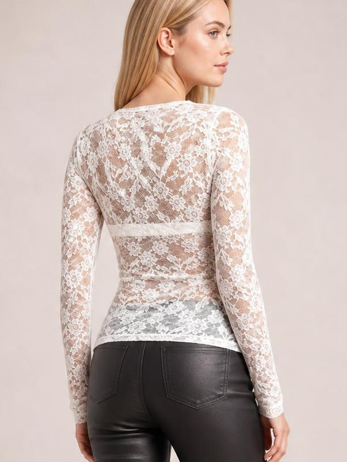 A model looks over her shoulder wearing a fitted white sheer lace top with long sleeves, floral construction, and a gently curved hem.