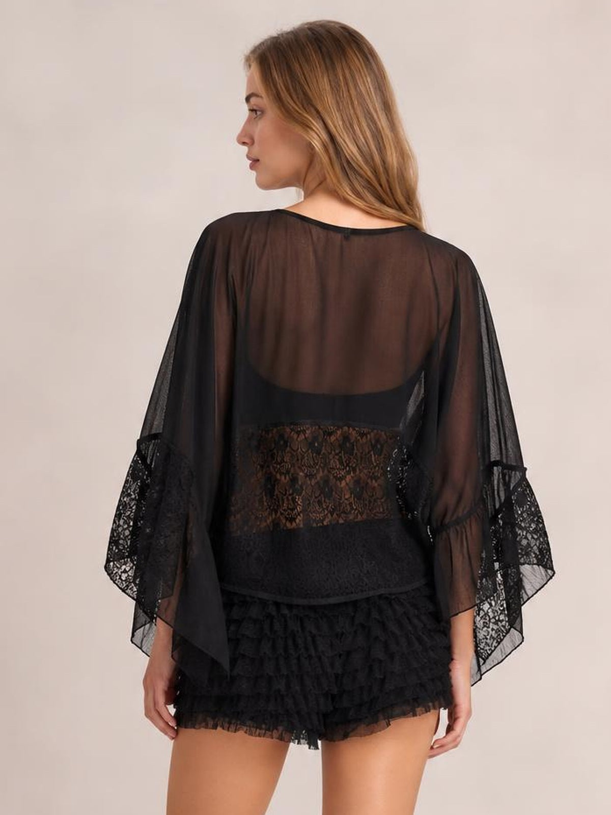 A model poses with her back turned in a black sheer lace long sleeve cover-up featuring flared sleeves and delicate lace panels for an airy silhouette.