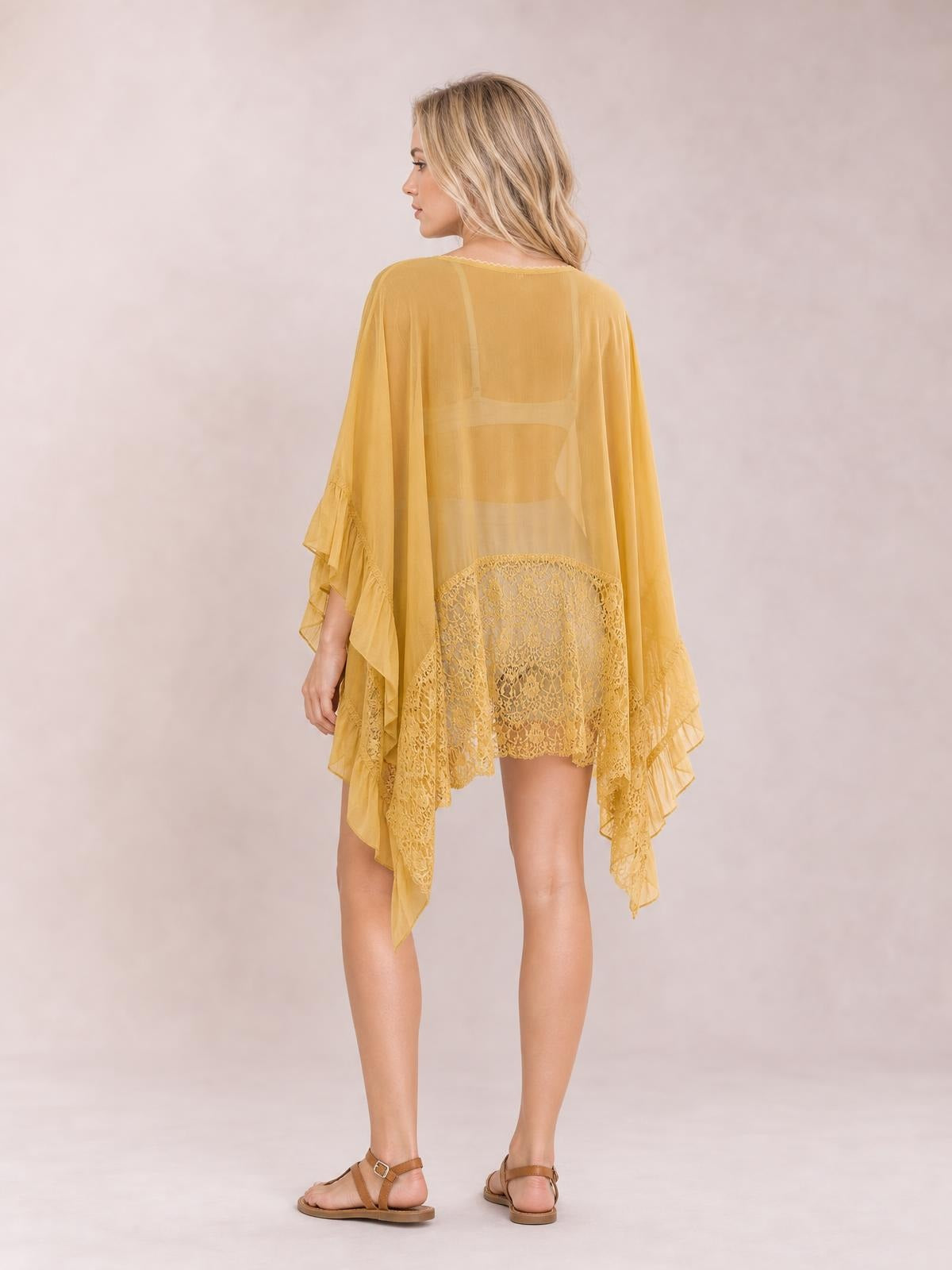 Model shown from behind wears a mustard-yellow lace cover-up with long sleeves, sheer flowing silhouette, and layered ruffle trim along the asymmetrical hem.